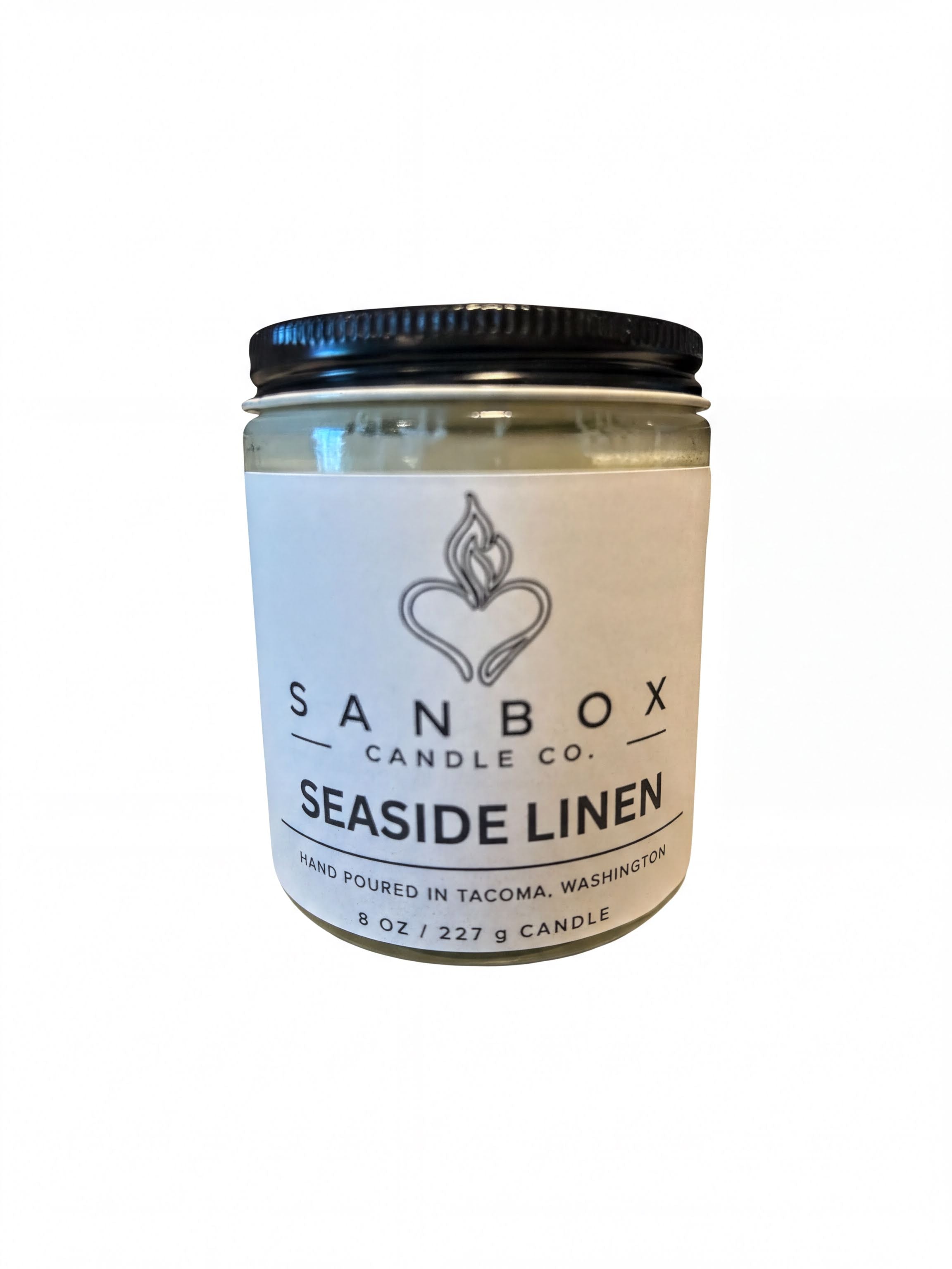 a jar of candle labeled "SANBOX CANDLE CO. SEASIDE LINEN" with a black lid.
