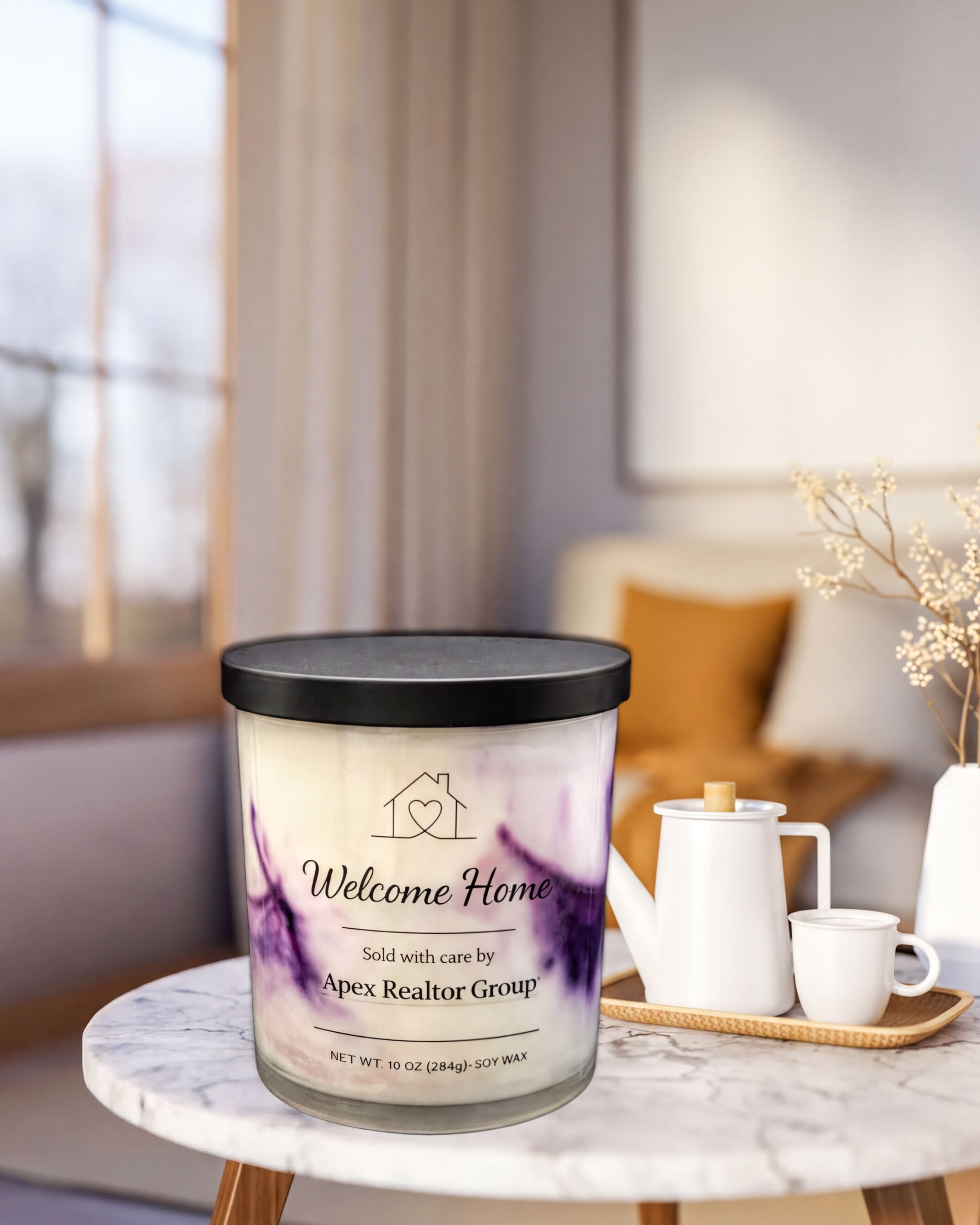 a candle labeled "Welcome Home" on a marble table, with a teapot and cups nearby.