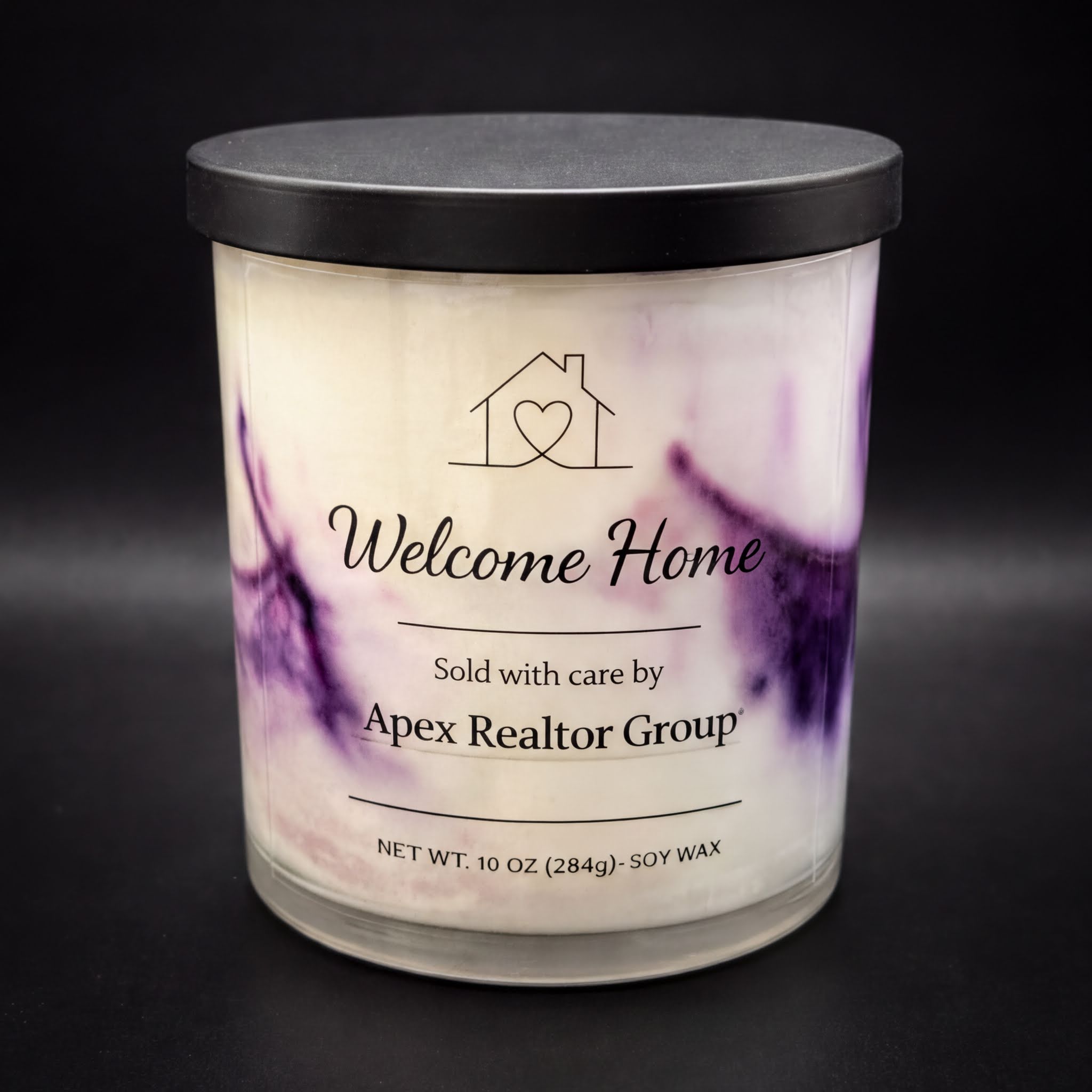 A white candle with purple swirls on it, labeled as a "Welcome Home" candle sold by the apex realtor group.