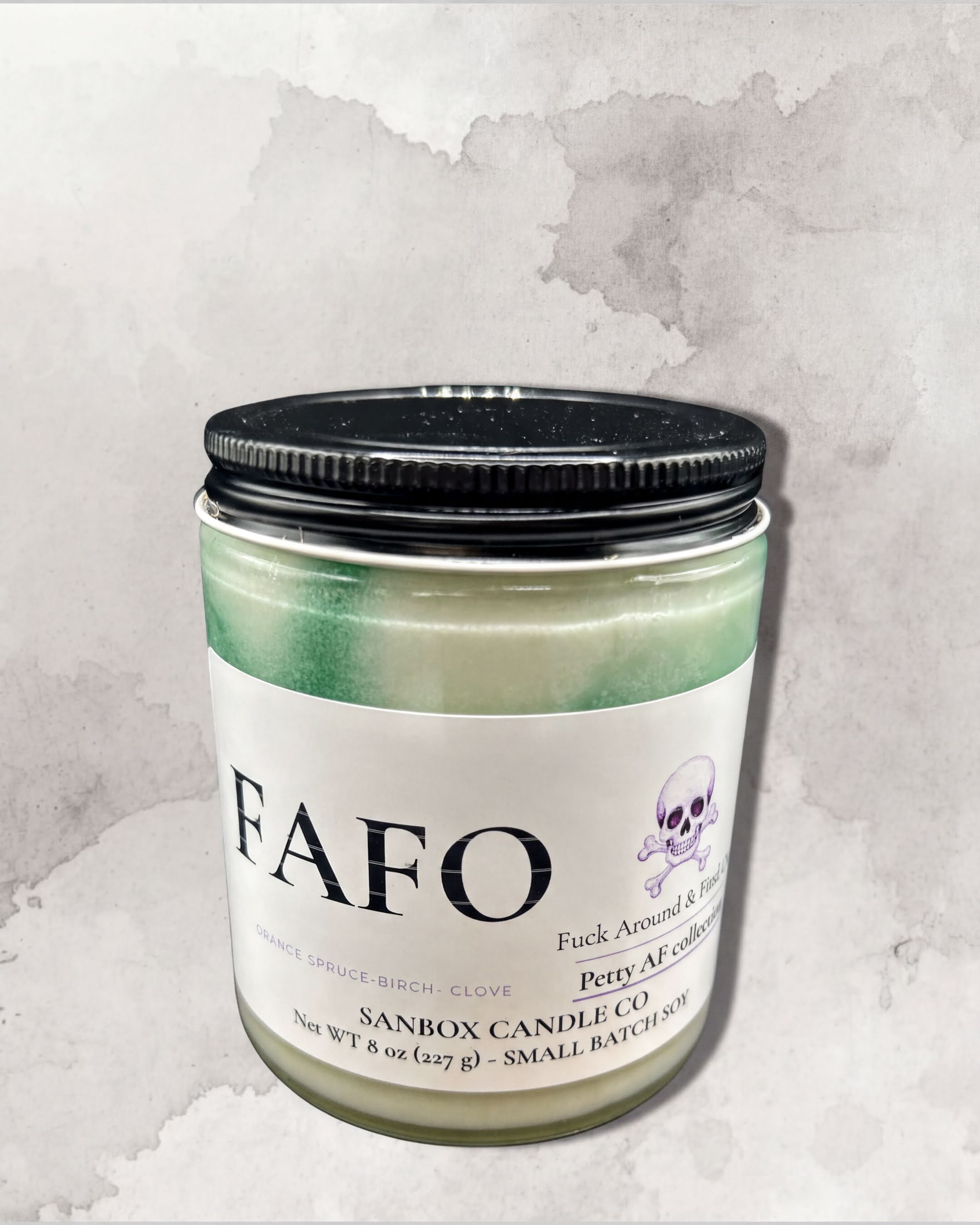 a candle labeled "FAFO" with a skull and crossbones design, placed against a watercolor background.