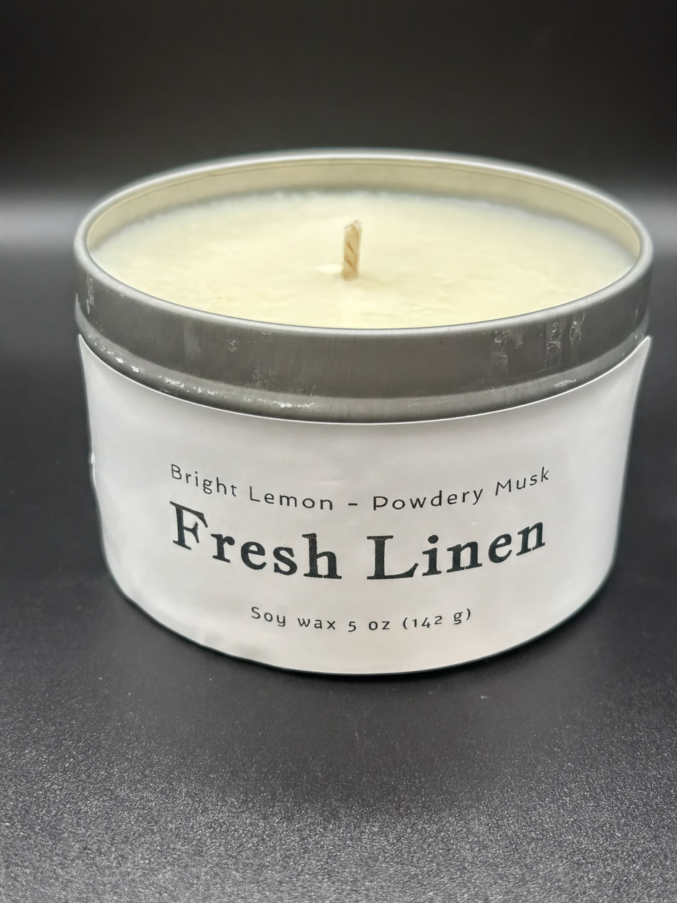 Fresh Linen scented soy wax candle in a metal tin, labeled bright lemon and powdery musk, 5oz size