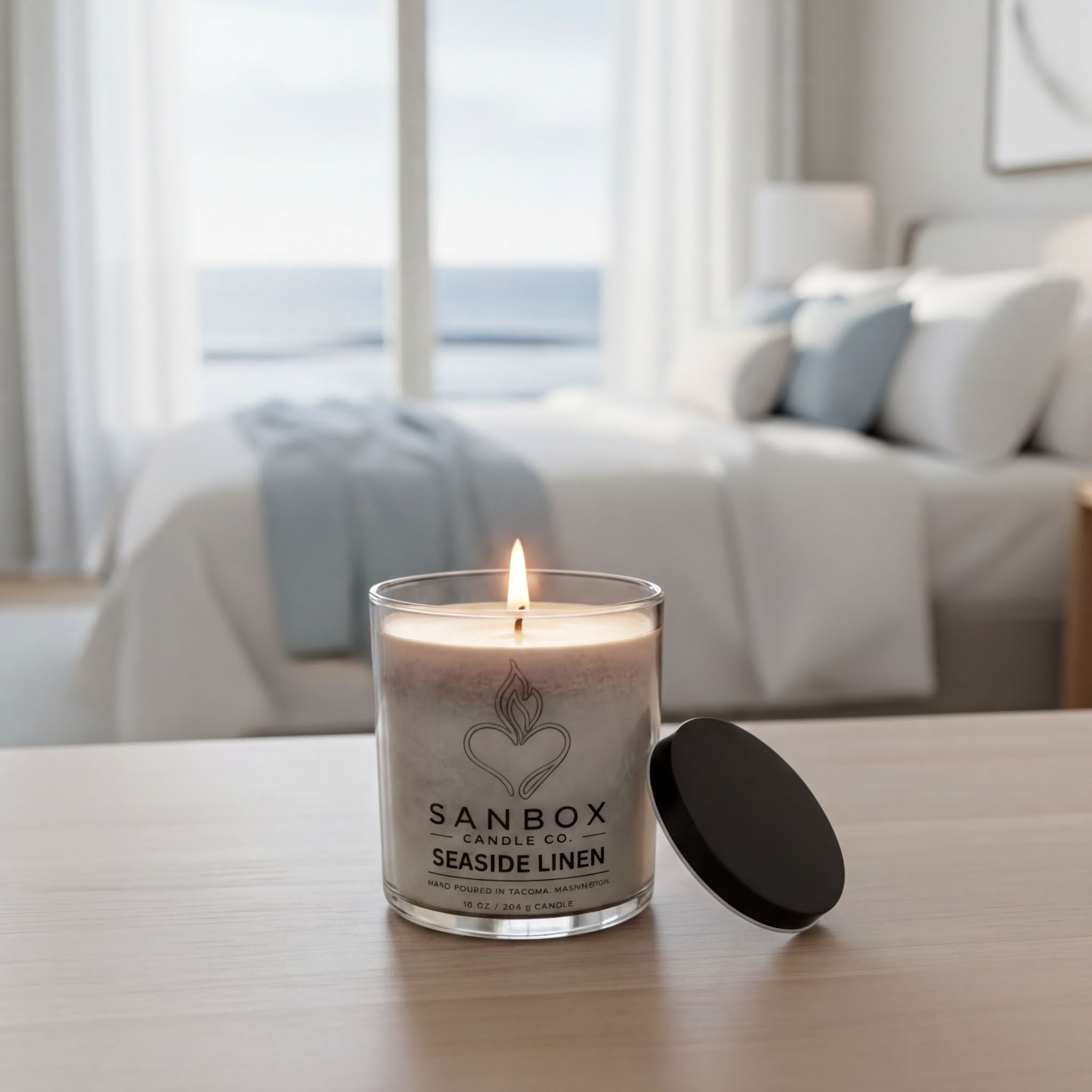 A lit candle in a glass container sits on a wooden surface, with a bedroom scene visible in the background.