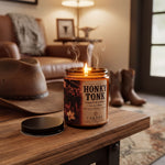 a lit candle on a wooden table, with a pair of cowboy boots and a hat visible in the background.