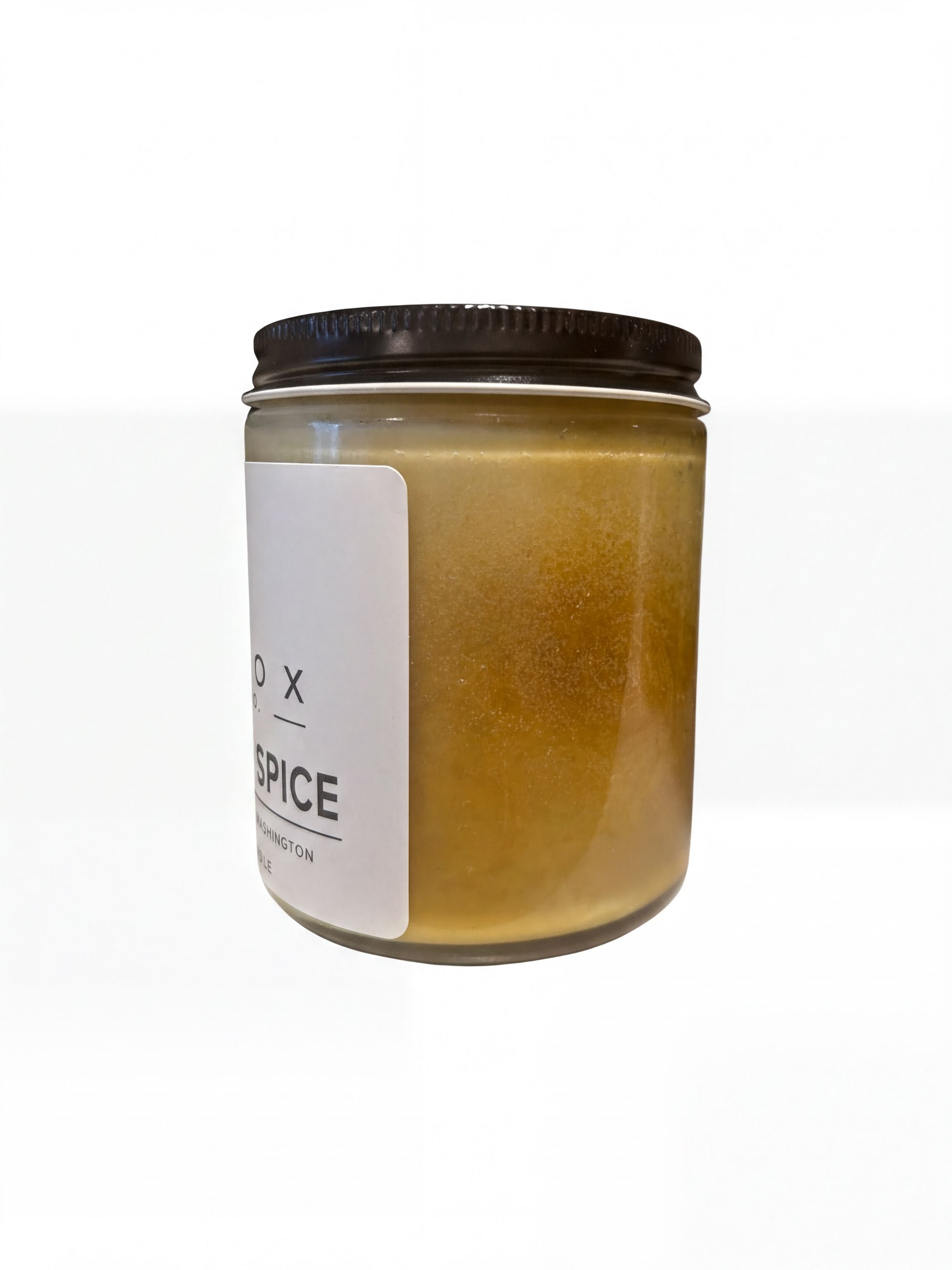 A glass jar with a black lid, containing a yellowish substance, possibly a candle or soap.