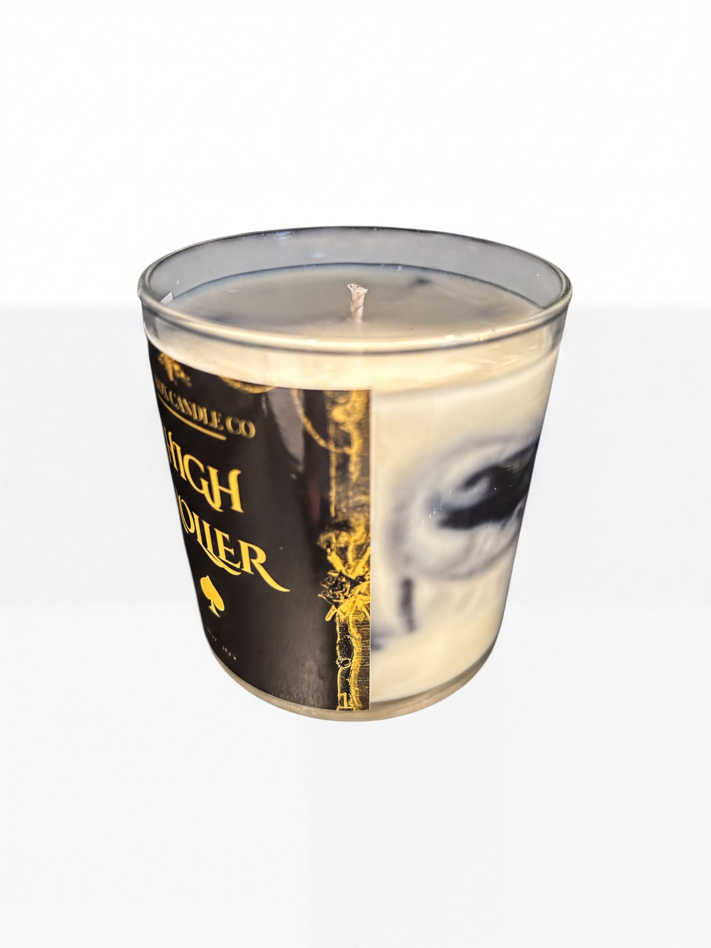 a candle in a glass container with a label that includes text and an eye design.