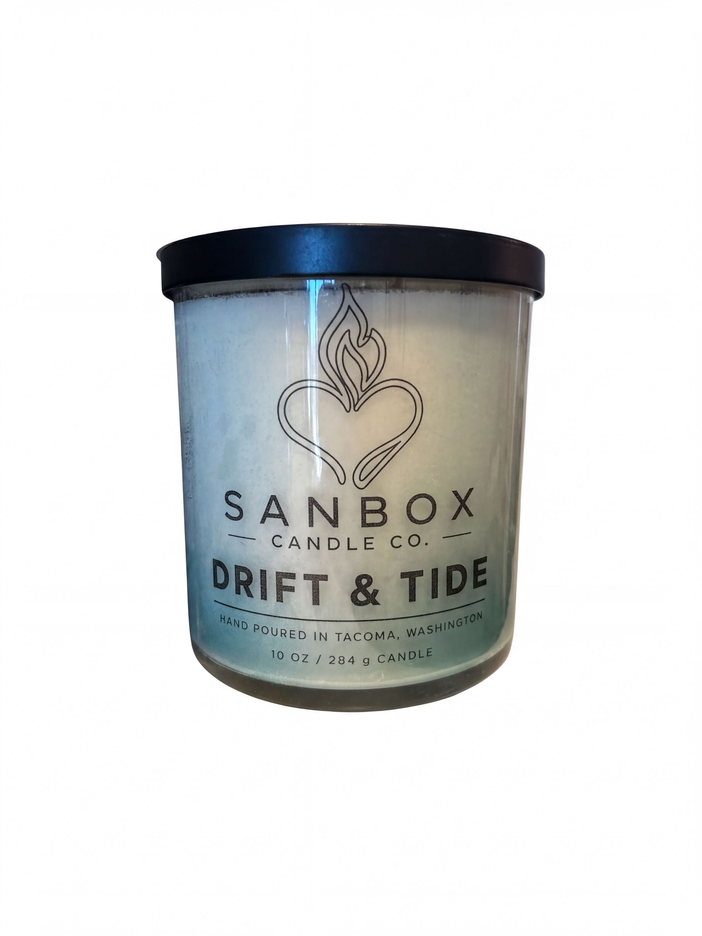 a cylindrical candle labeled "Drift & Tide" from Sanbox Candle Co. The candle is hand-poured in Tama, Washington and contains 10 fluid ounces (284 mL) of wax.