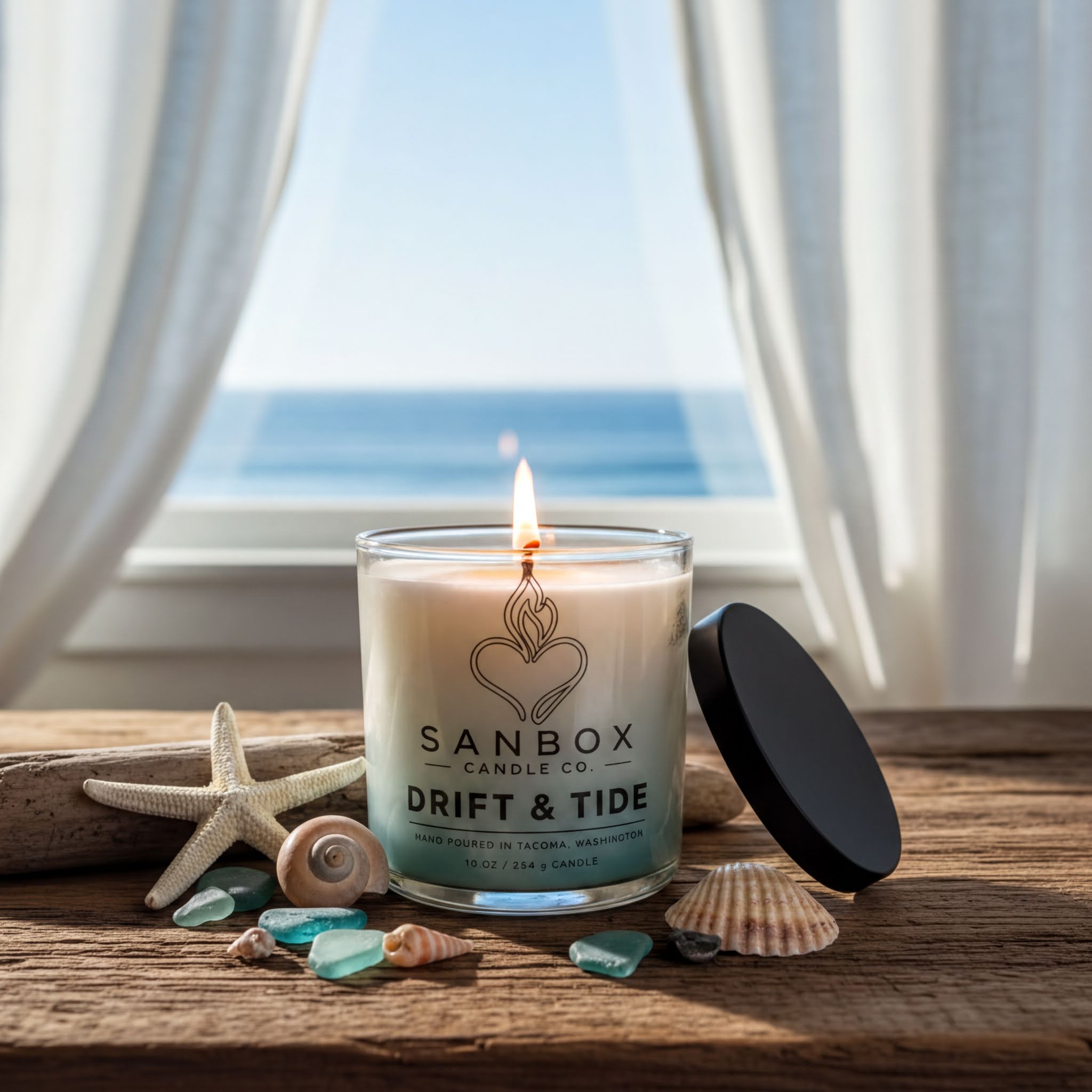 a candle labeled "Drift & Tide" on a wooden surface, with a lit candle and various seashells and starfish nearby. The scene is set against a backdrop of a window overlooking the ocean.