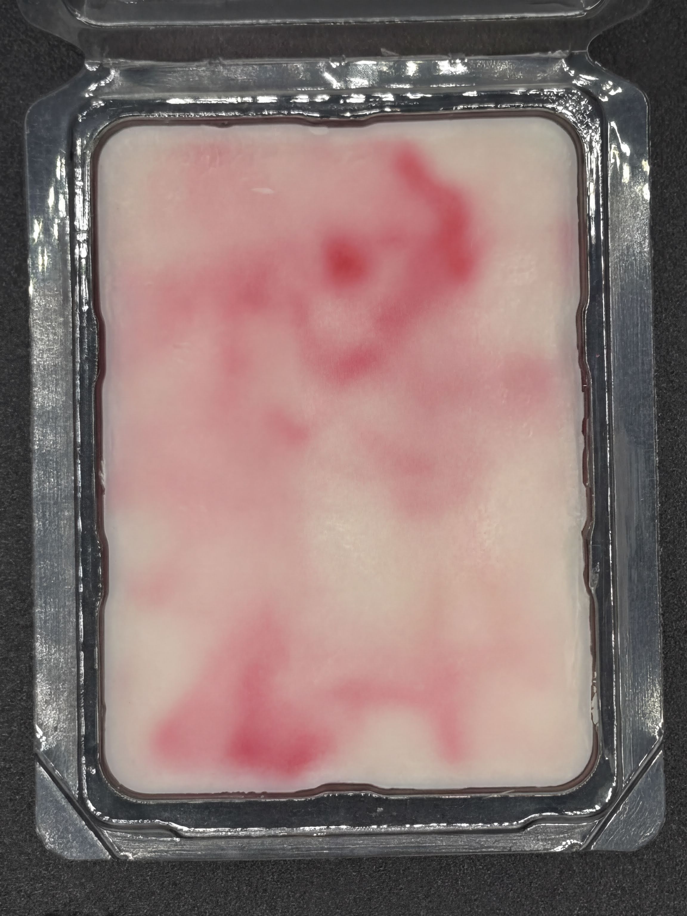 Hand-poured pink and white wax melt in clear plastic clamshell on dark surface