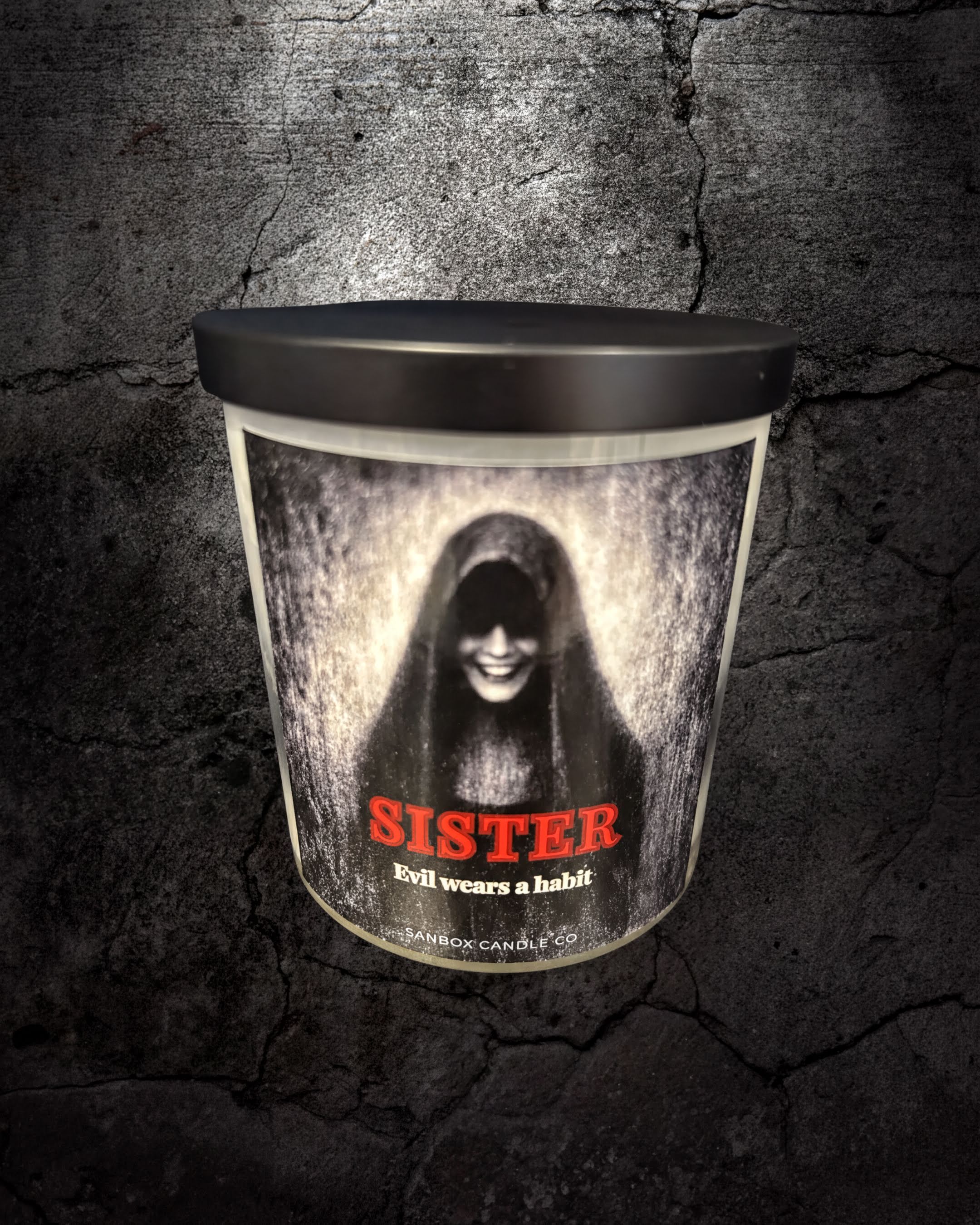 A cylindrical candle holder with a black lid and a printed design featuring a woman's face and the word "SISTER" in red text.