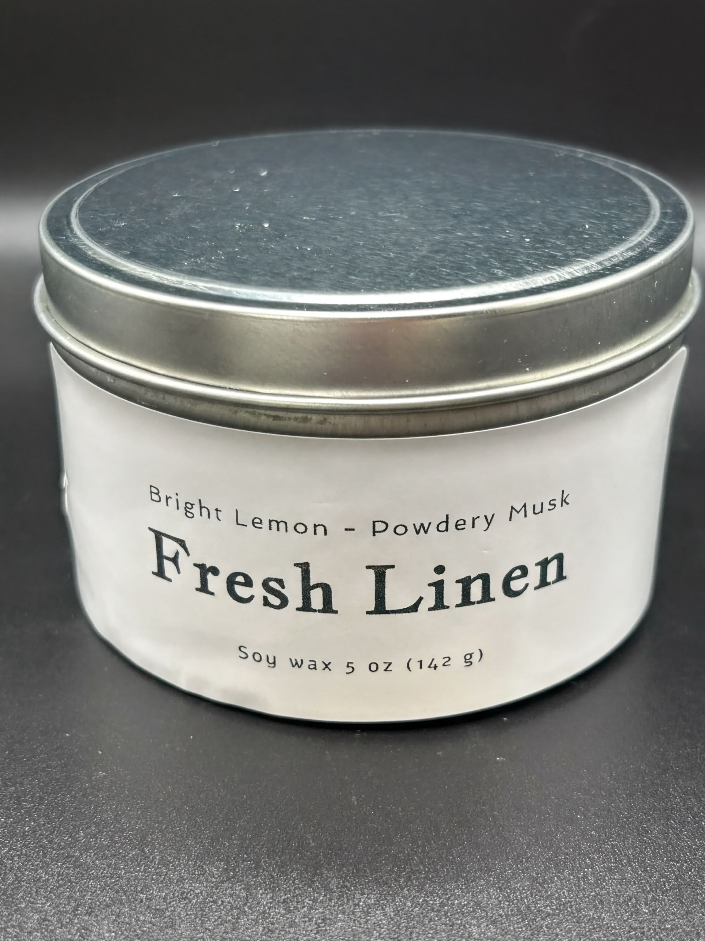 Fresh Linen soy wax candle in a metal tin, labeled bright lemon and powdery musk scent, 5oz.