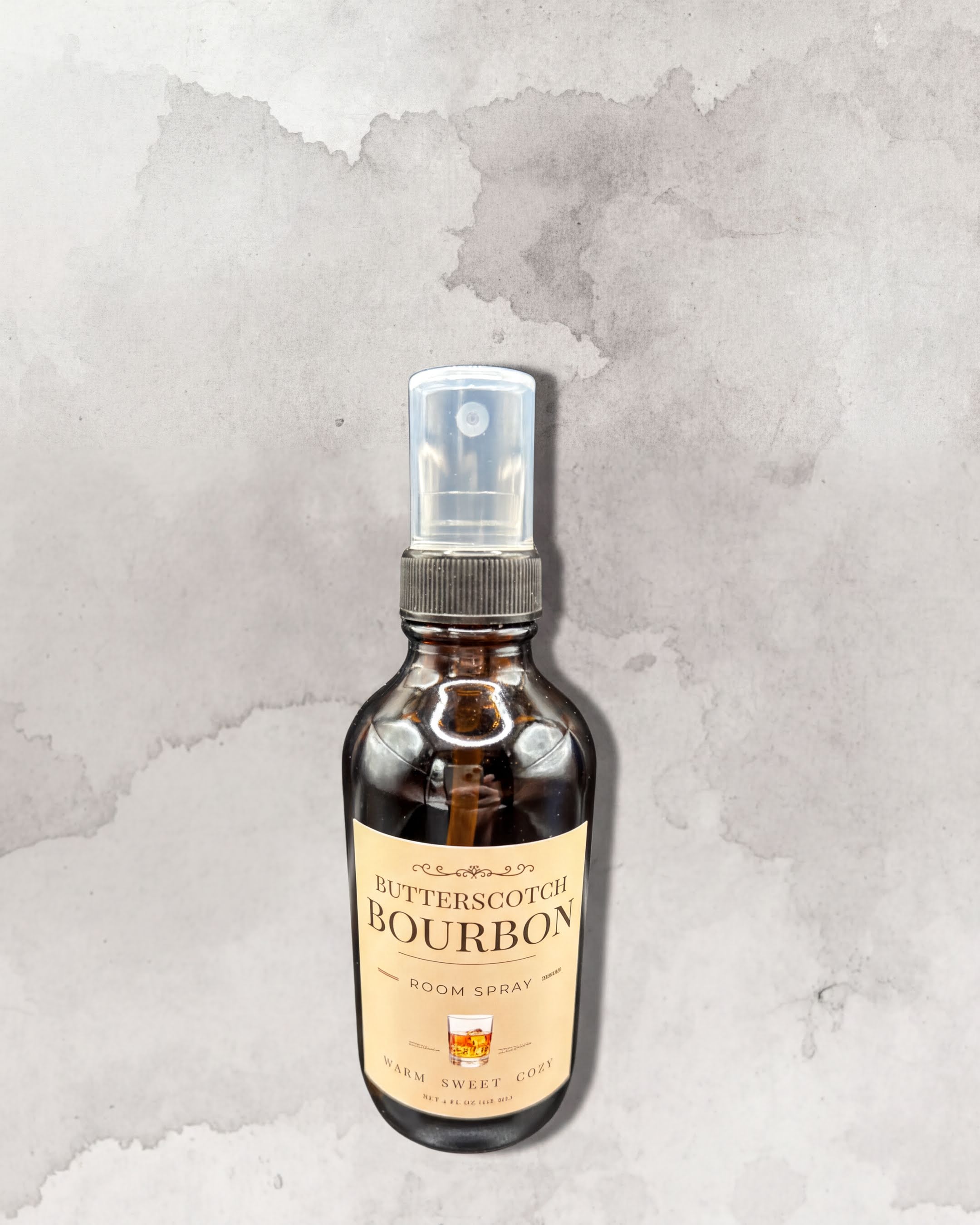 A bottle of Butterscotch Bourbon room spray against a textured gray background.