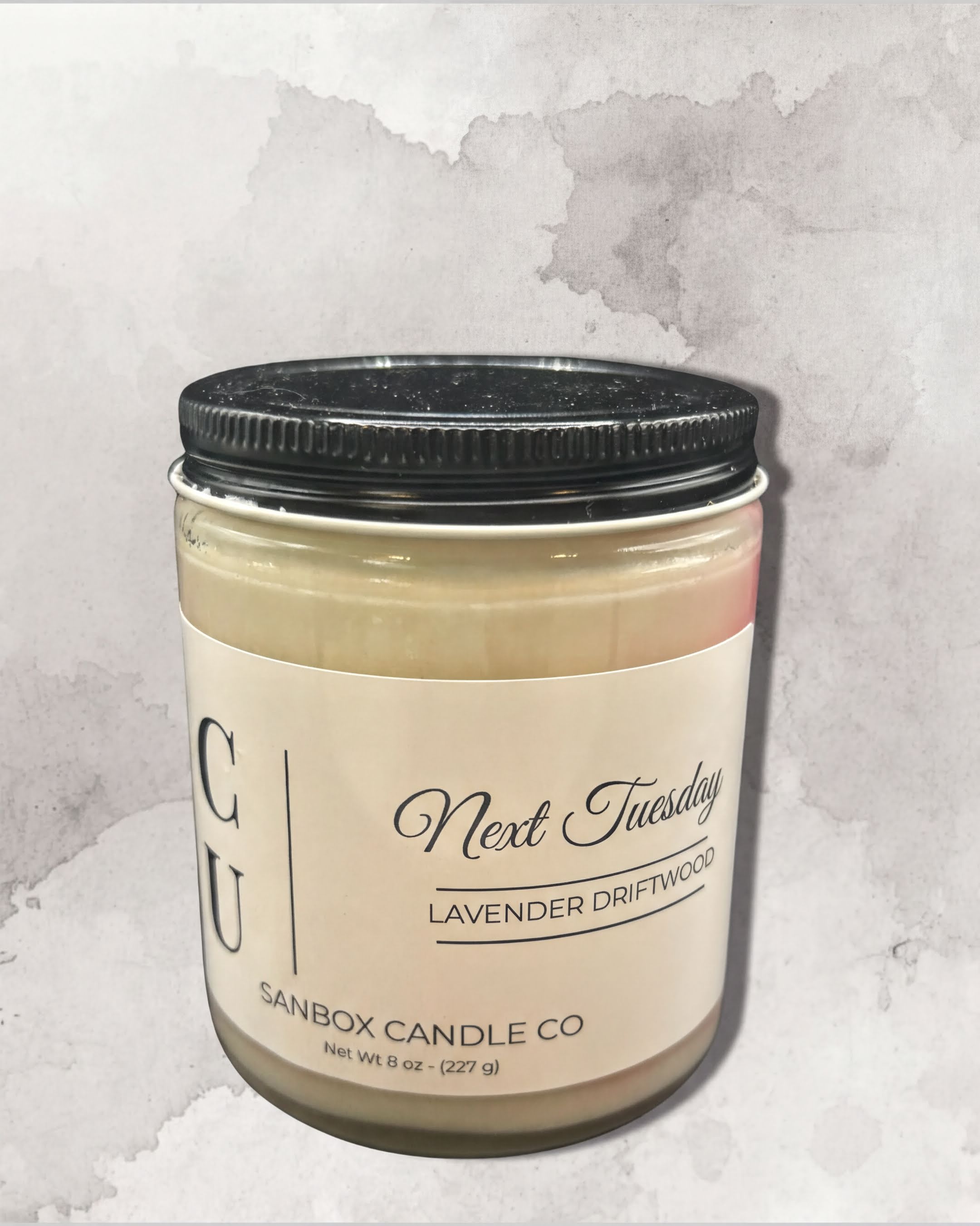 a jar of lavender-scented candle with a black lid, set against a textured gray background.