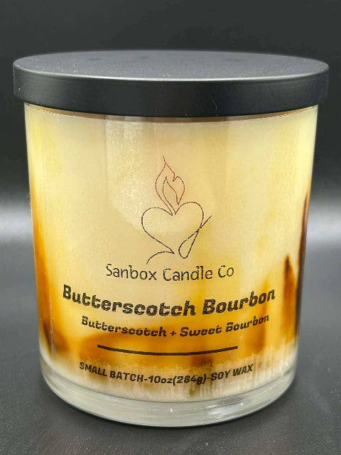 10 ounce Butterscotch Bourbon Candle with lid on a dark background from Sanbox Candle