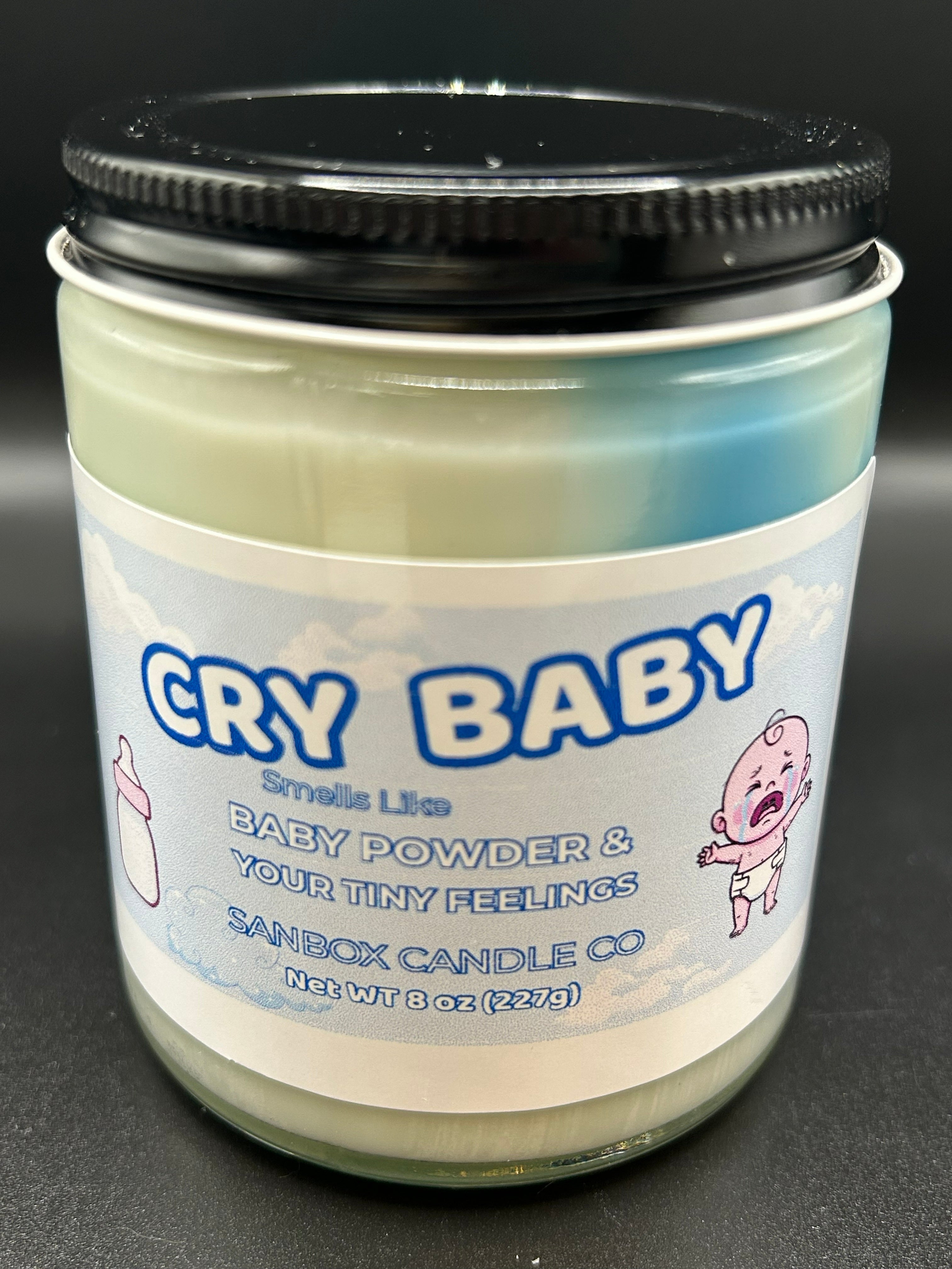 8oz scented candle in glass jar with black lid, blue label, and crying baby cartoon design.