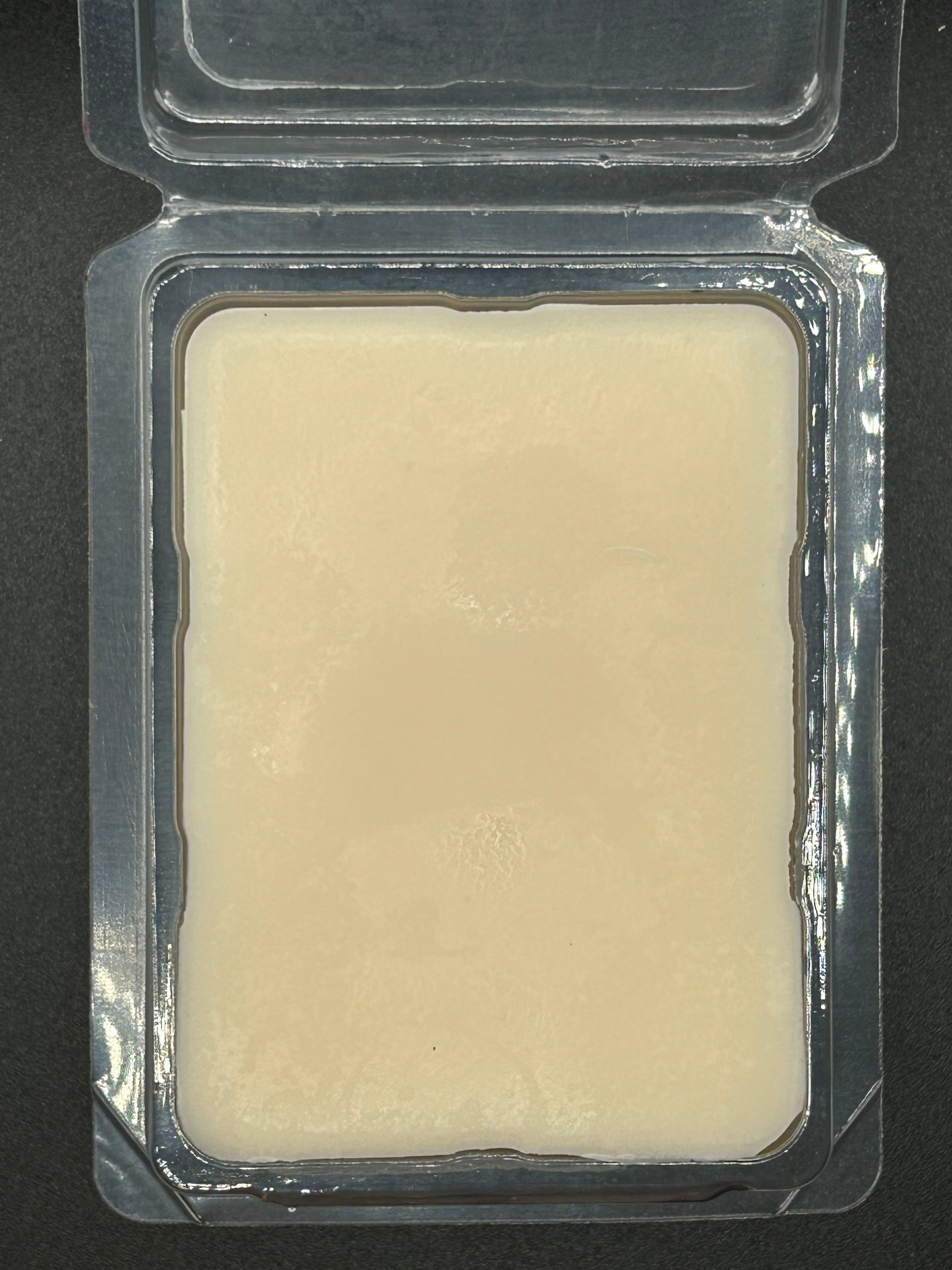 Hand-poured scented wax melt in clear plastic clamshell packaging on dark background