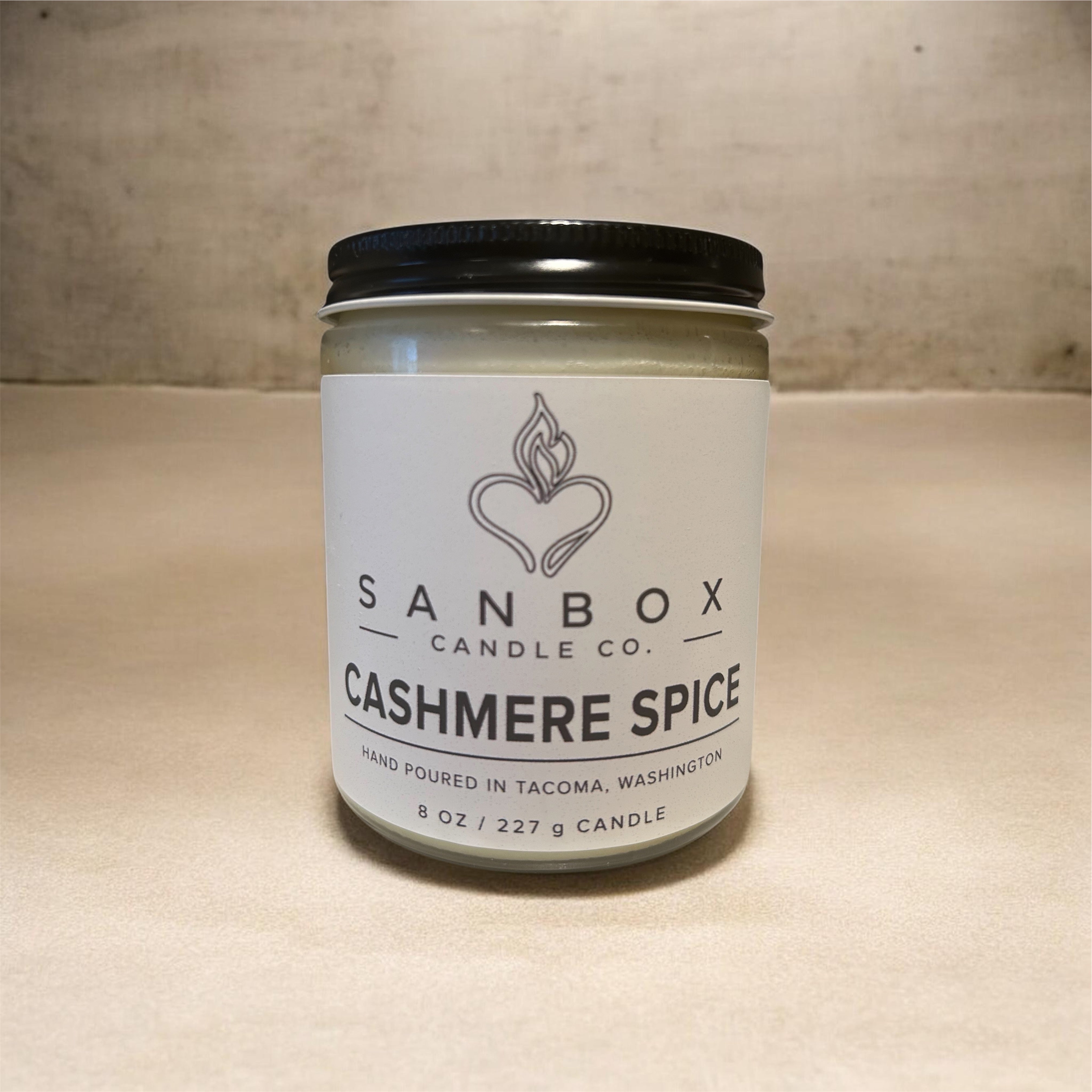 A jar of Sanbox Candle Co. Cashmere Spice candle is displayed on a countertop.