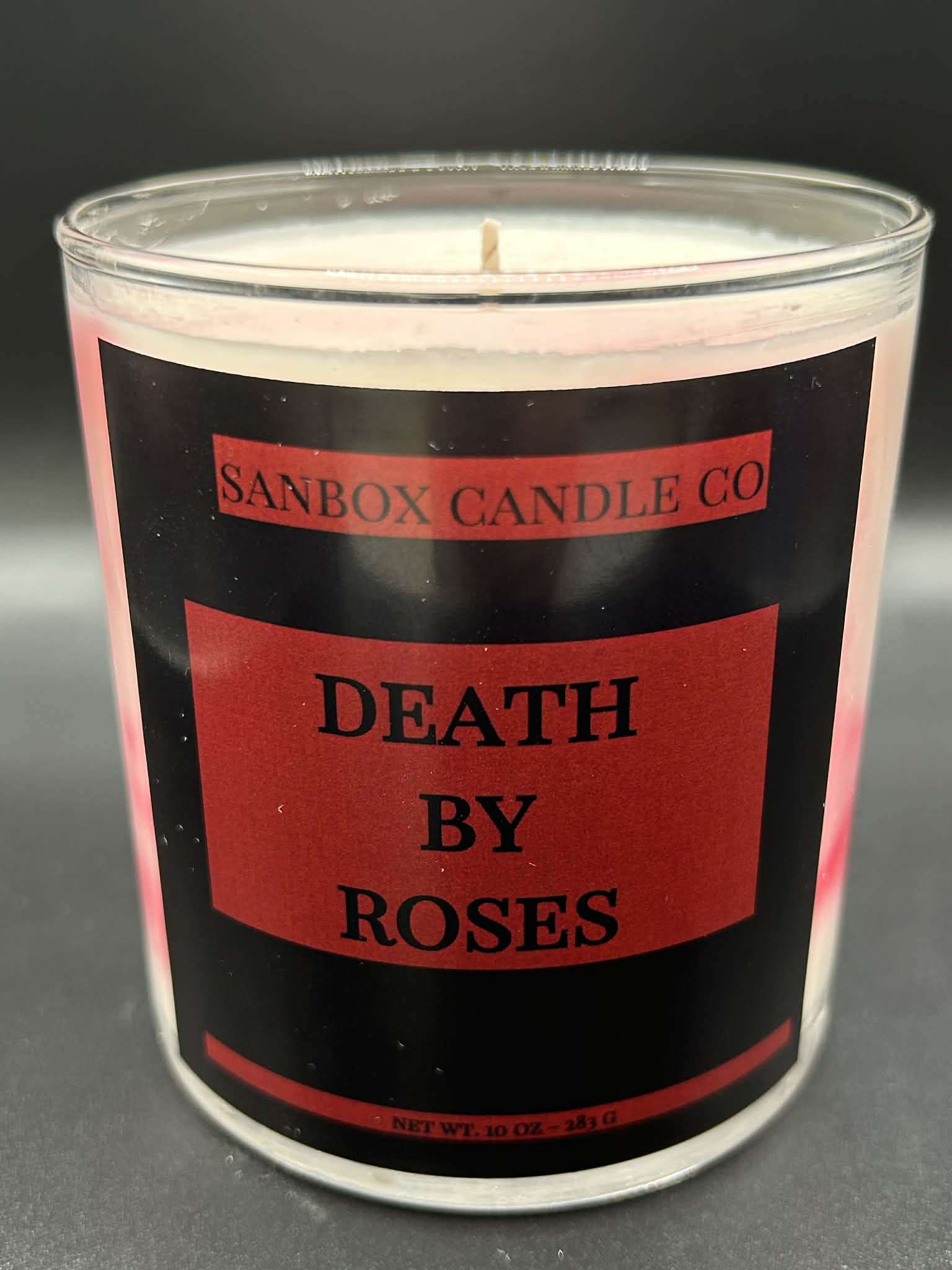 10oz hand-poured scented candle labeled Death By Roses in clear glass jar on black background