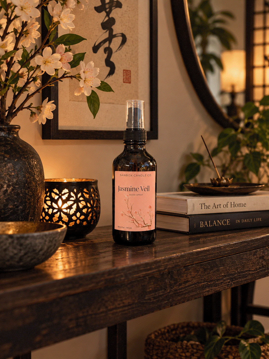 Jasmine Veil jasmine floral room spray in an amber bottle with a blush pink label, styled on a dark wood console beside jasmine blossoms 