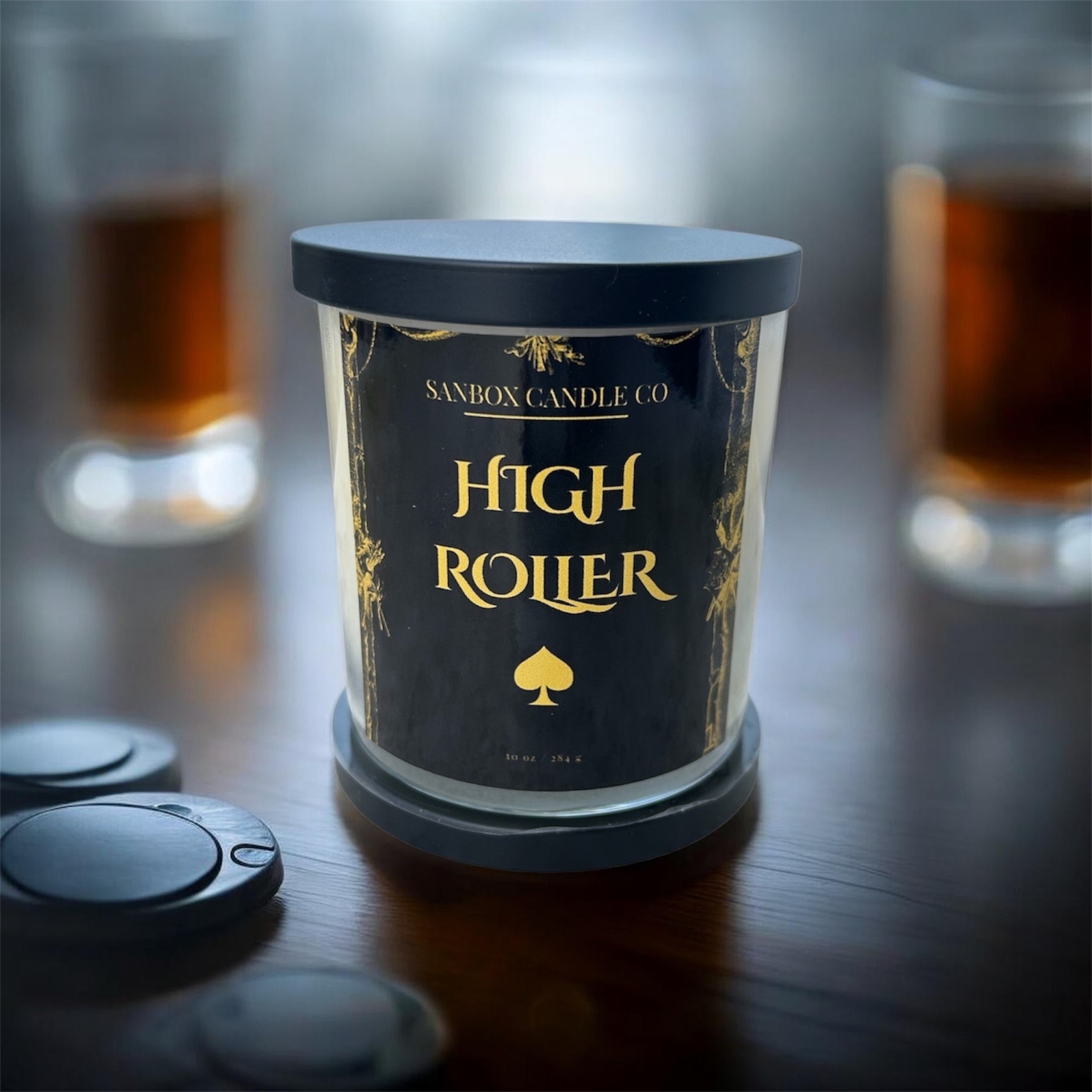 A candle labeled "High Roller" in gold text, with a spade symbol, sits on a table surrounded by other objects.
