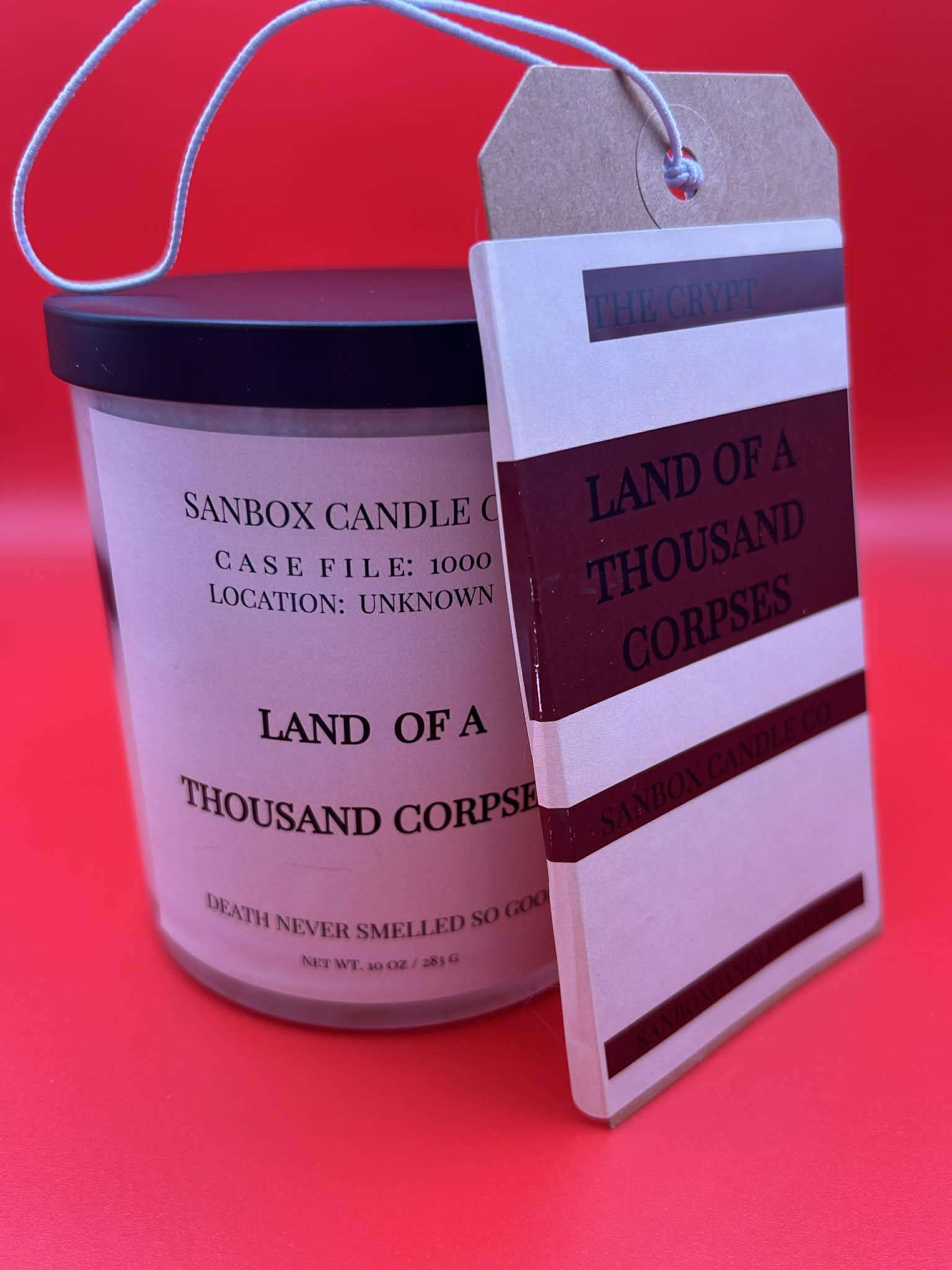 Hand-poured scented candle labeled 'Land of a Thousand Corpses' with matching tag on red background