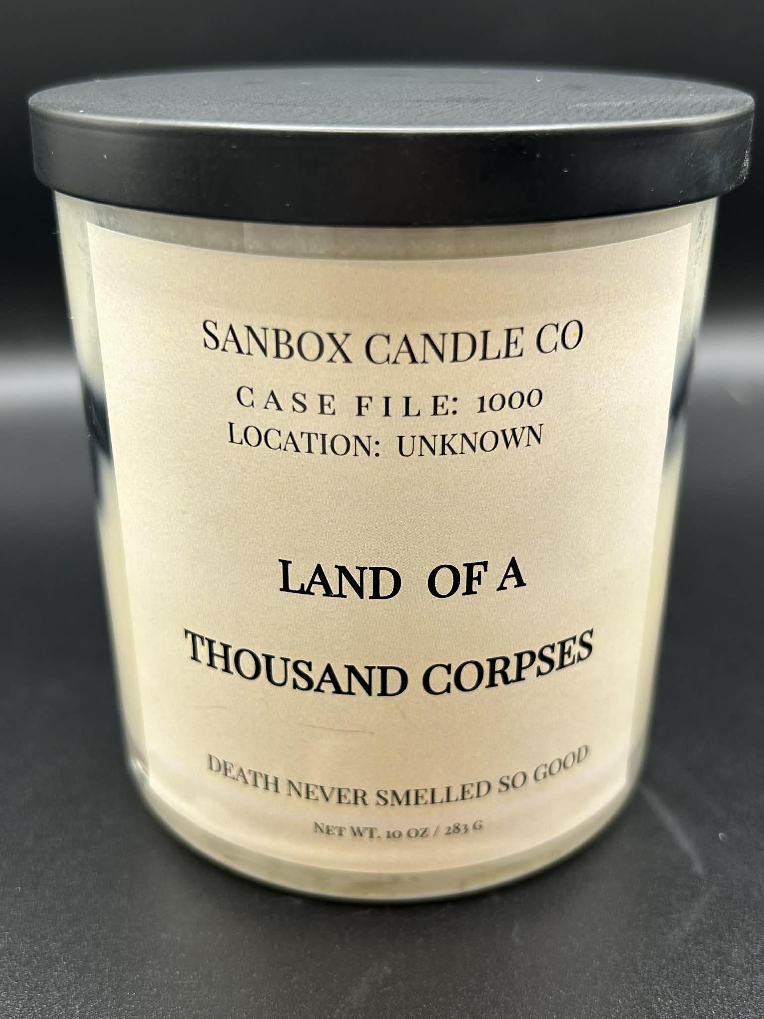 Scented soy candle in glass jar with black lid, label reads 'Land of a Thousand Corpses', 10oz.