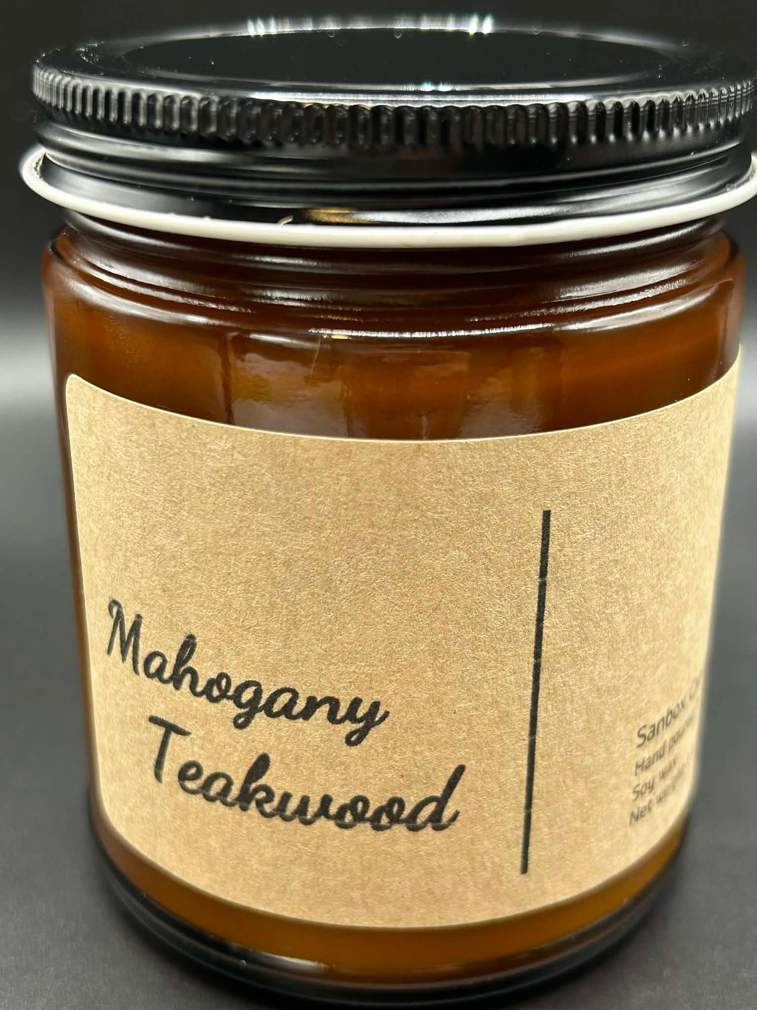 Mahogany Teakwood scented candle in amber glass jar with black lid on black background