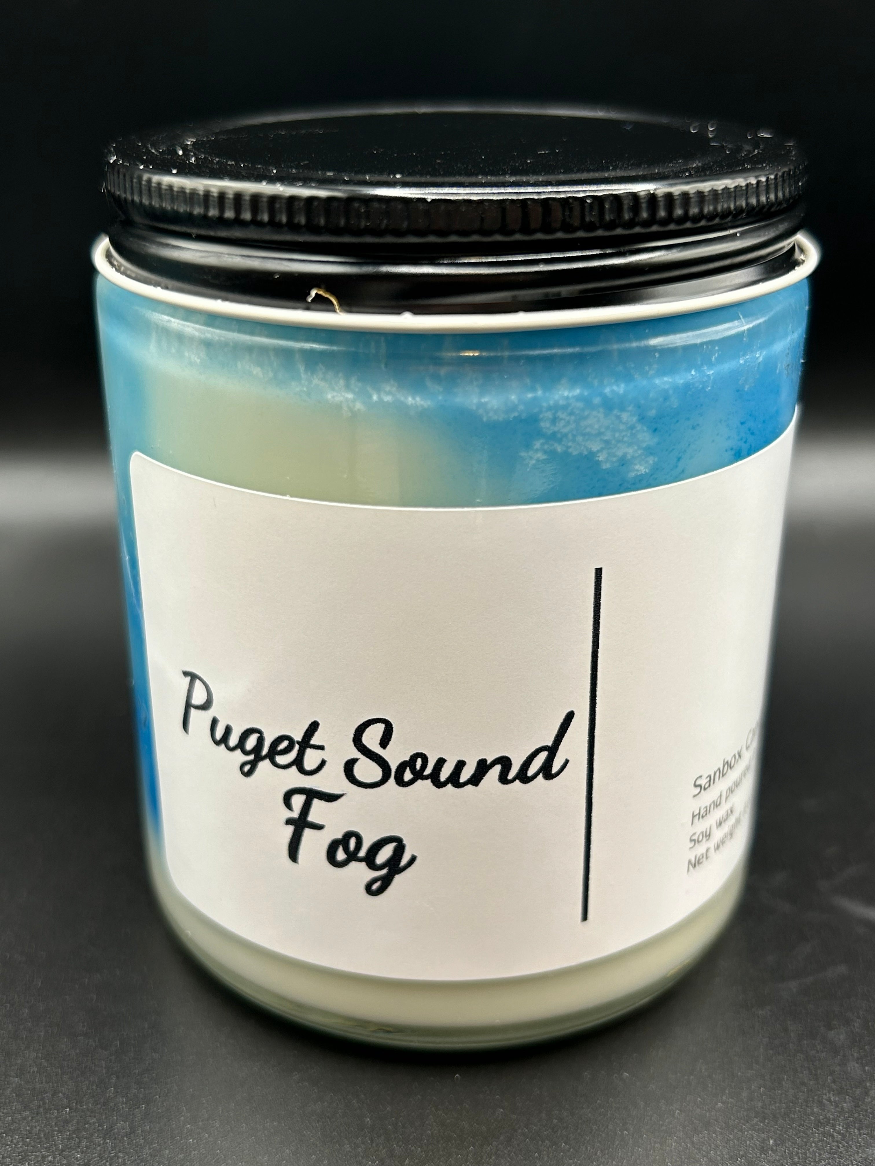 Puget Sound Fog scented candle in a glass jar with black lid and blue wax design