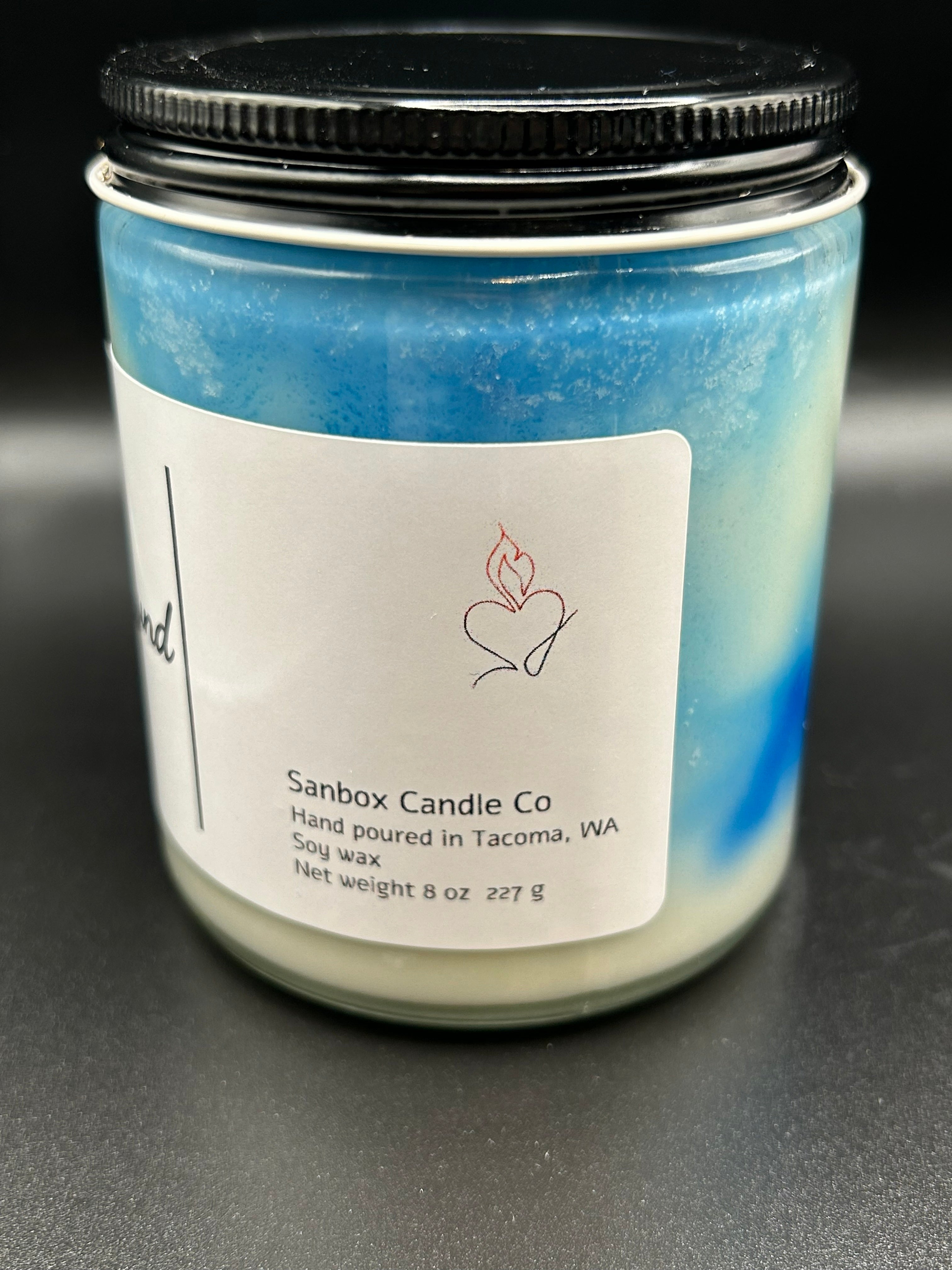 Hand-poured blue and white soy candle in glass jar with black lid, 8oz, product label visible.
