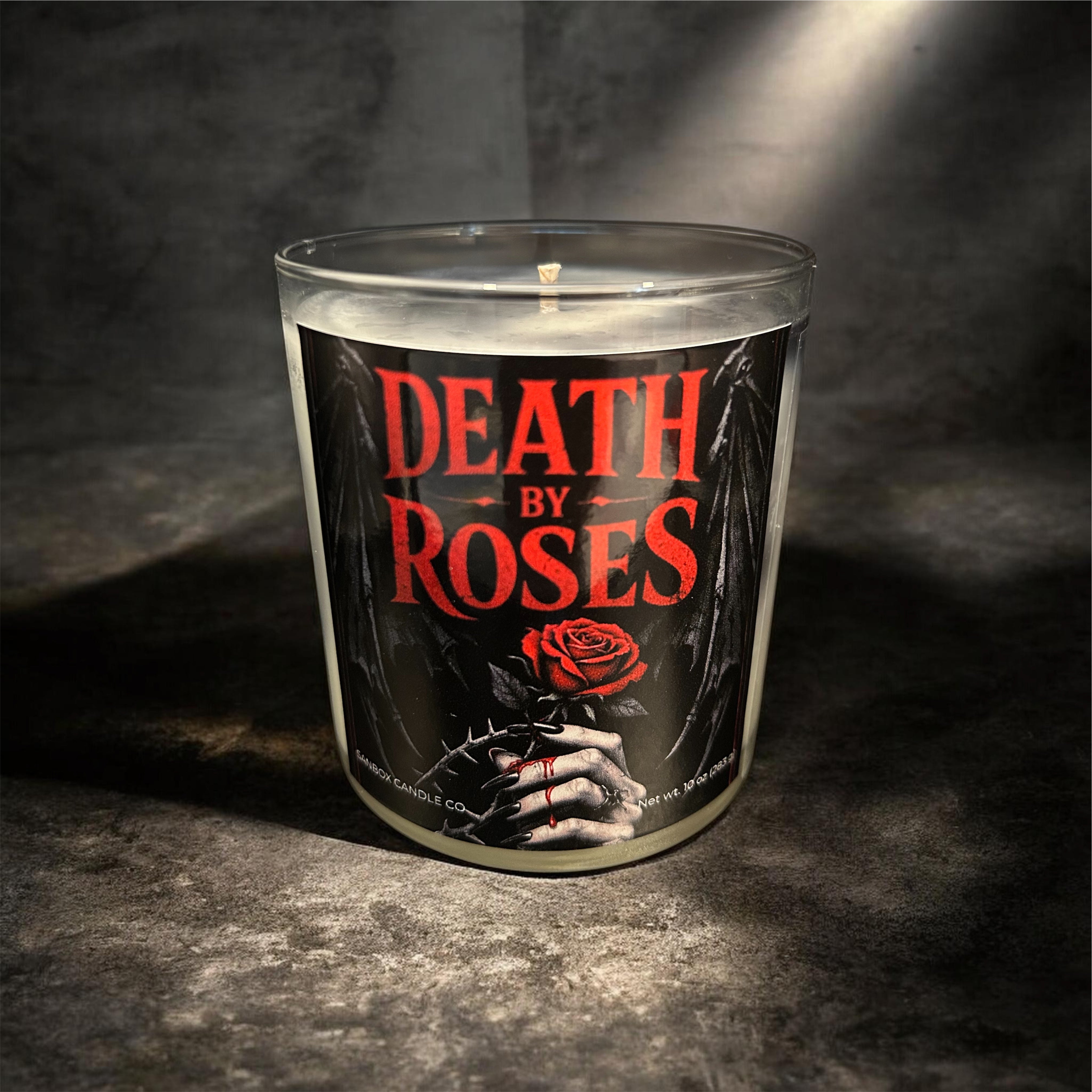 a candle with a dark, moody design and the text "DEATH BY ROSES" prominently displayed on it.