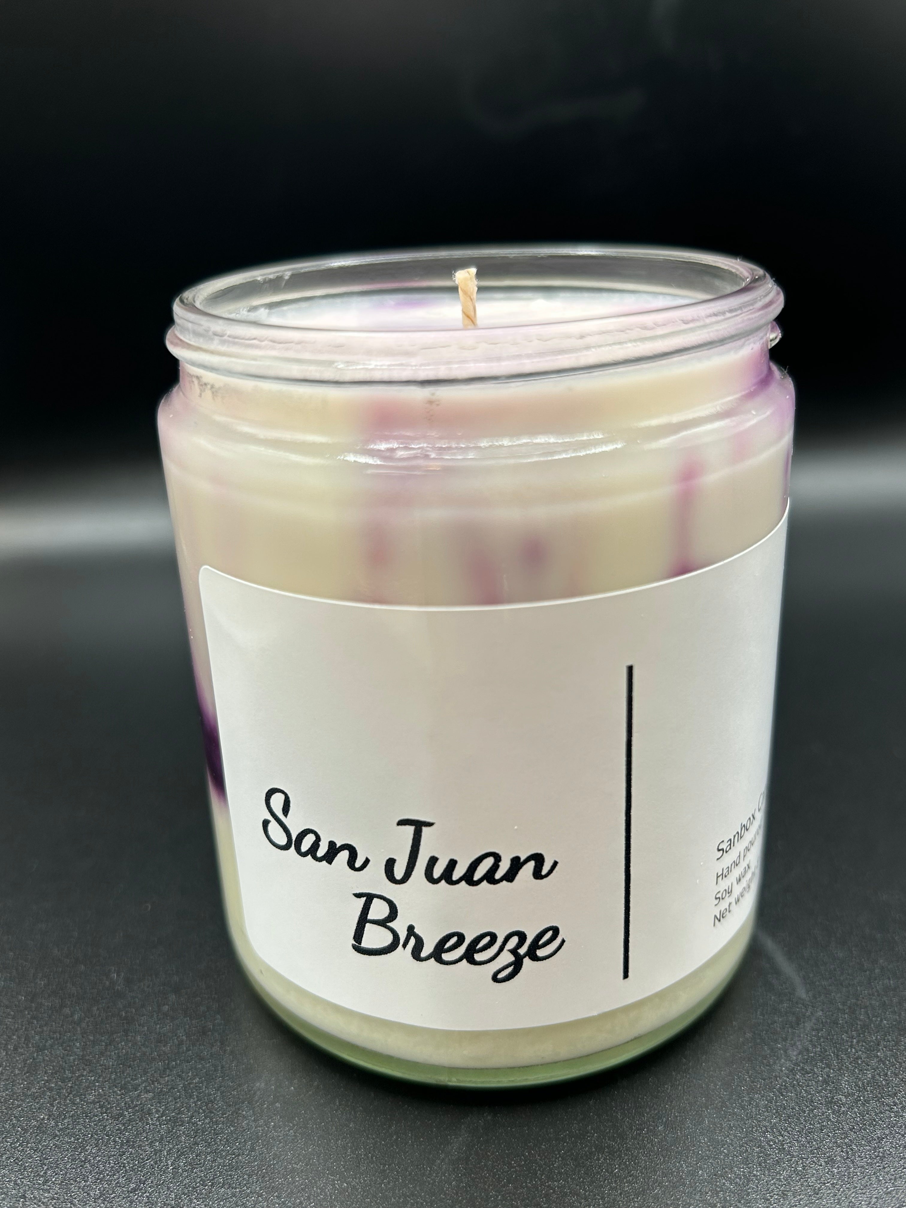 San Juan Breeze hand-poured scented candle in glass jar with purple accents on black background