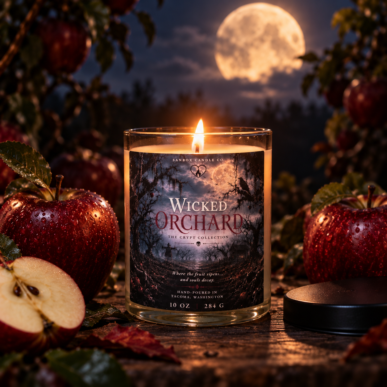 Wicked Orchard 10 oz apple amber soy candle burning in a clear glass jar with a black lid, surrounded by red apples, a skull, a raven, and vintage spell books in a gothic Halloween scene