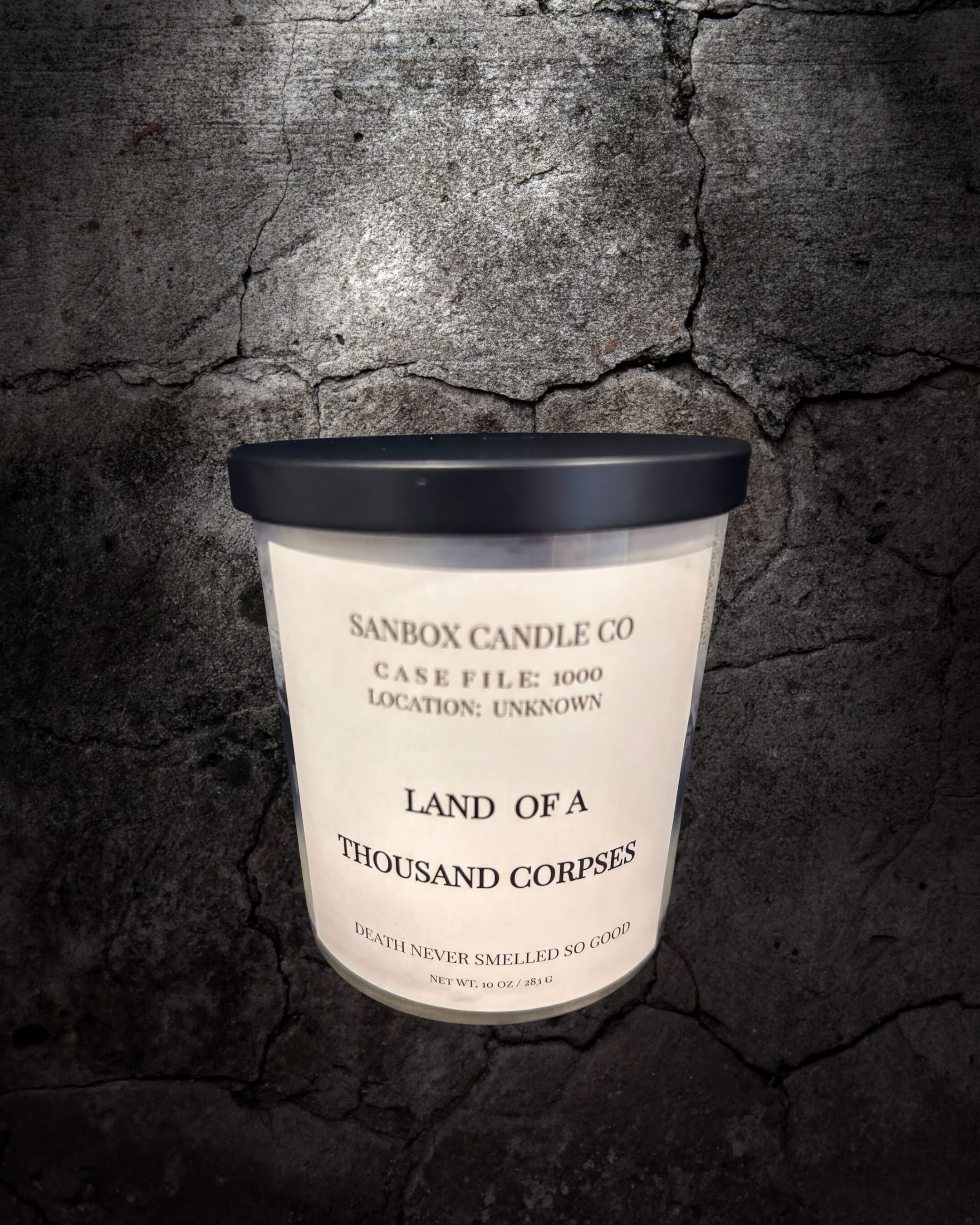 A candle labeled "Land of a Thousand Corpses" from the Sanbox Candle Co. against a dark, cracked background.
