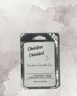 a rectangular, metallic, and silver-colored container with a label that reads "Obidian Obsessed Sanbox Candle Co."
