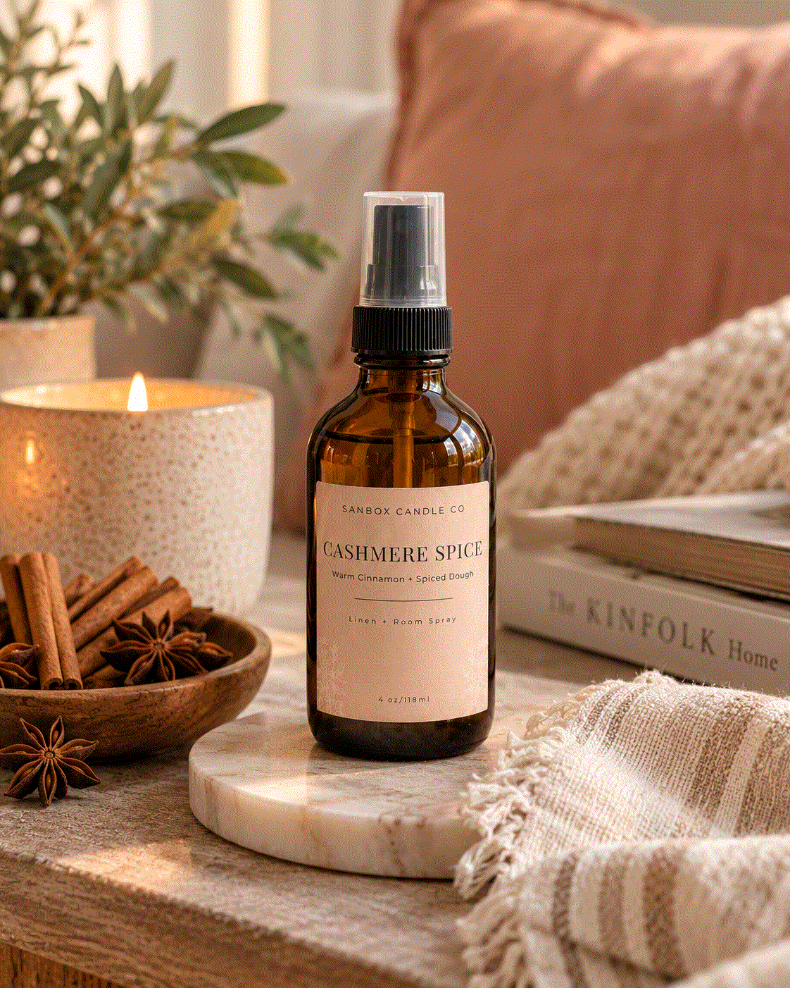 Sanbox Candle Co Cashmere Spice room spray bottle on a marble coaster in a cozy living room with a lit candle and throw blanket