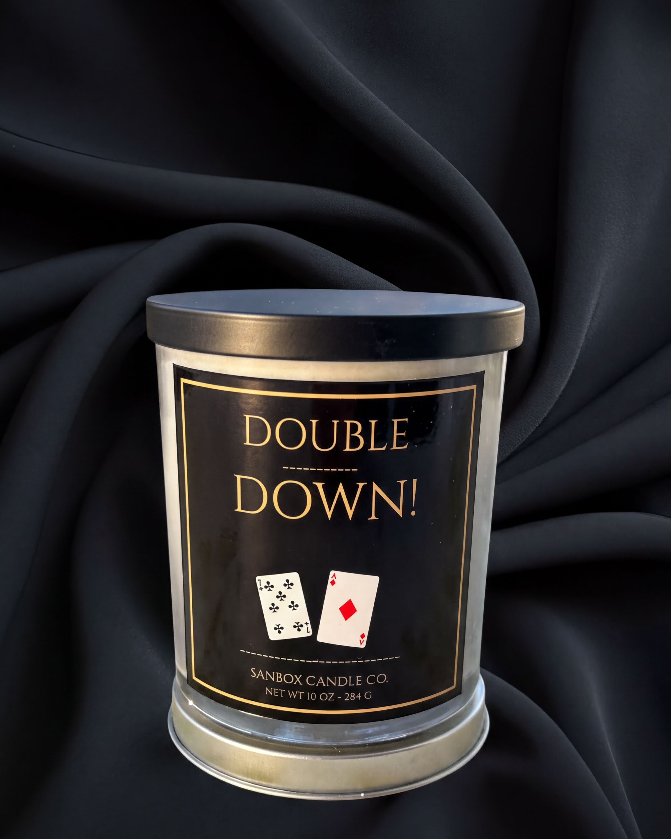 a candle labeled "Double Down!" with playing cards and text, placed on a dark fabric background.