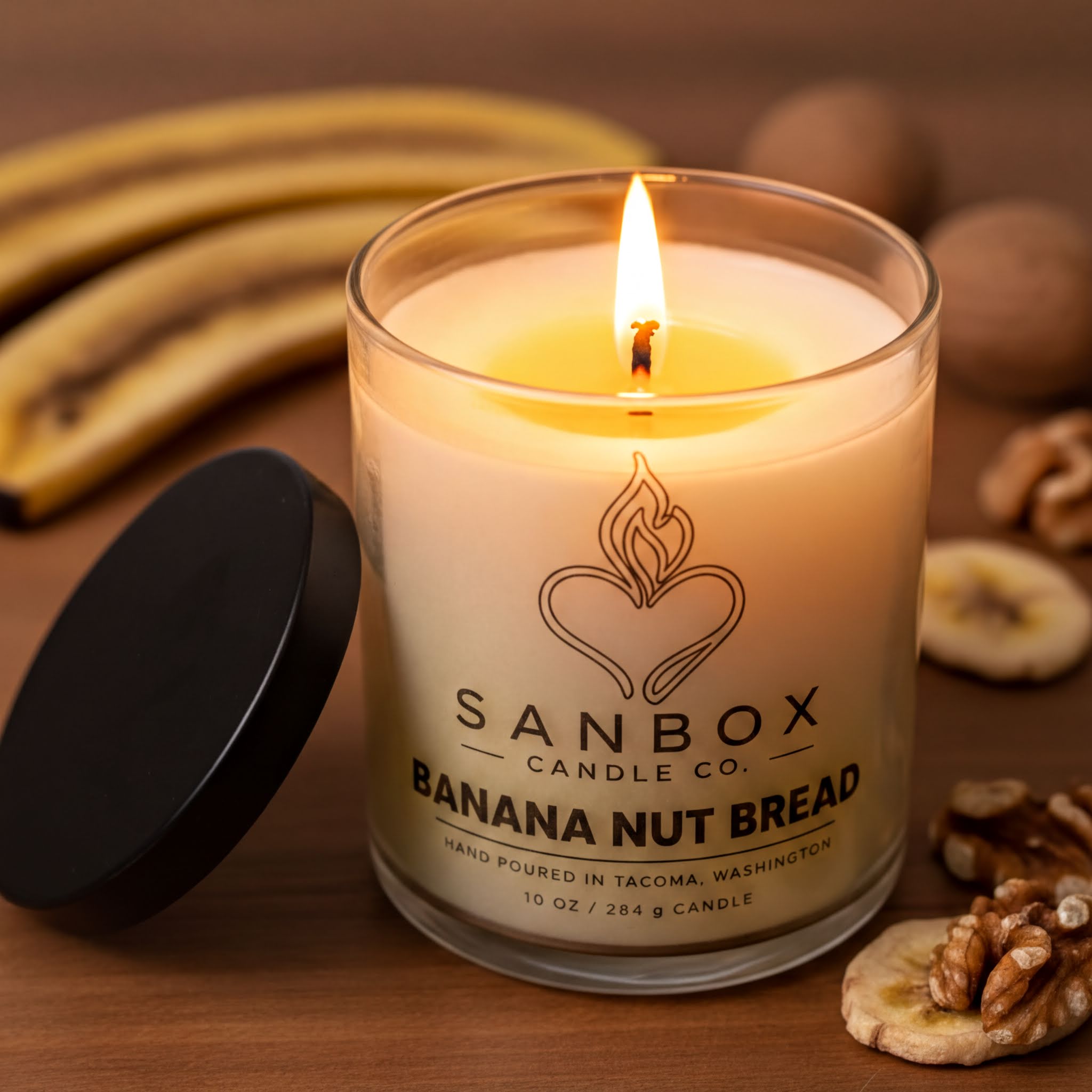 A lit candle in a glass jar with a black lid, surrounded by banana slices and walnuts on a wooden surface.