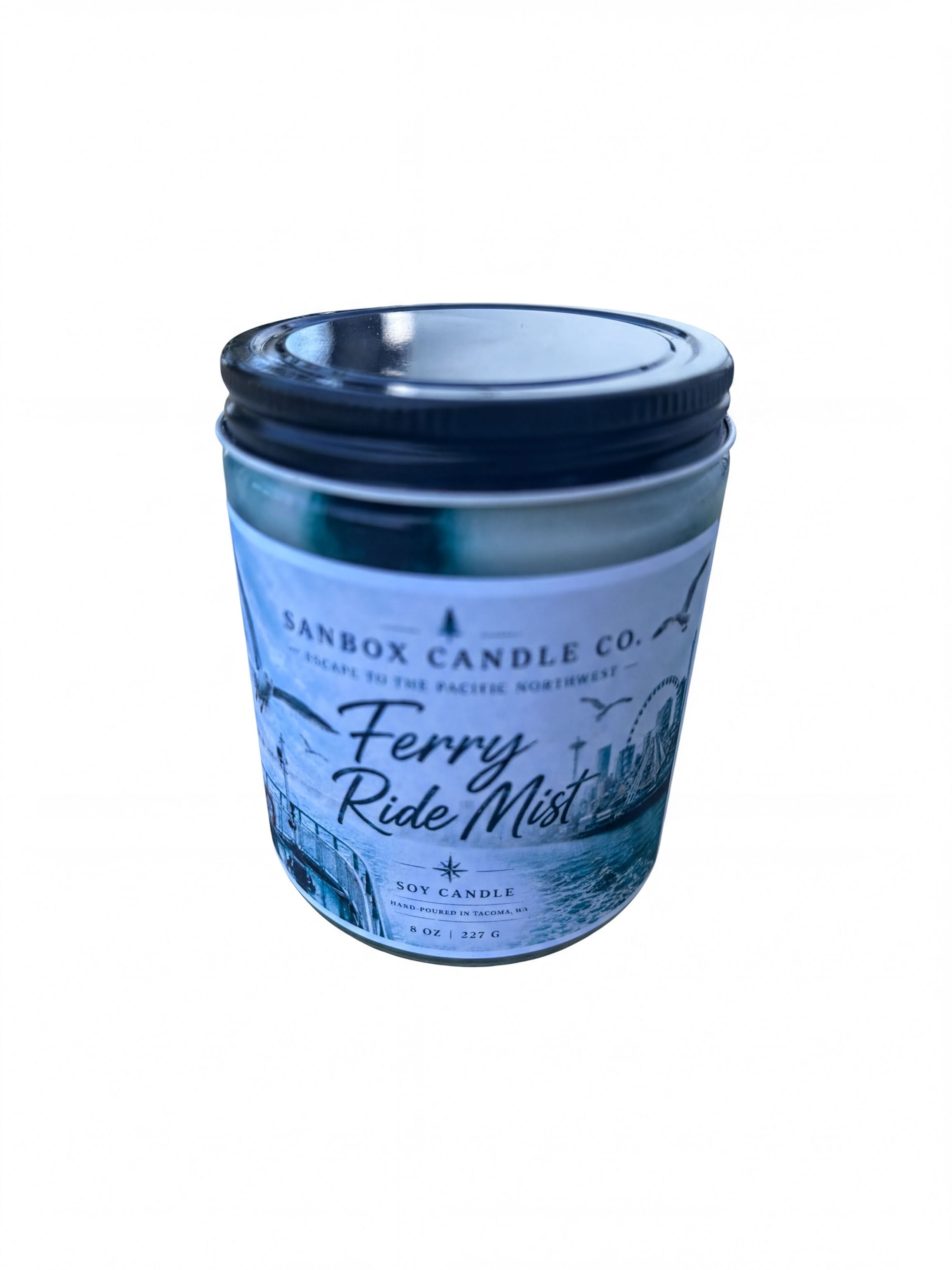 A cylindrical candle in a jar with a label that says "Ferry Ride Mist" and "SANBOX CANDLE CO. Escape to the Pacific Northwest".