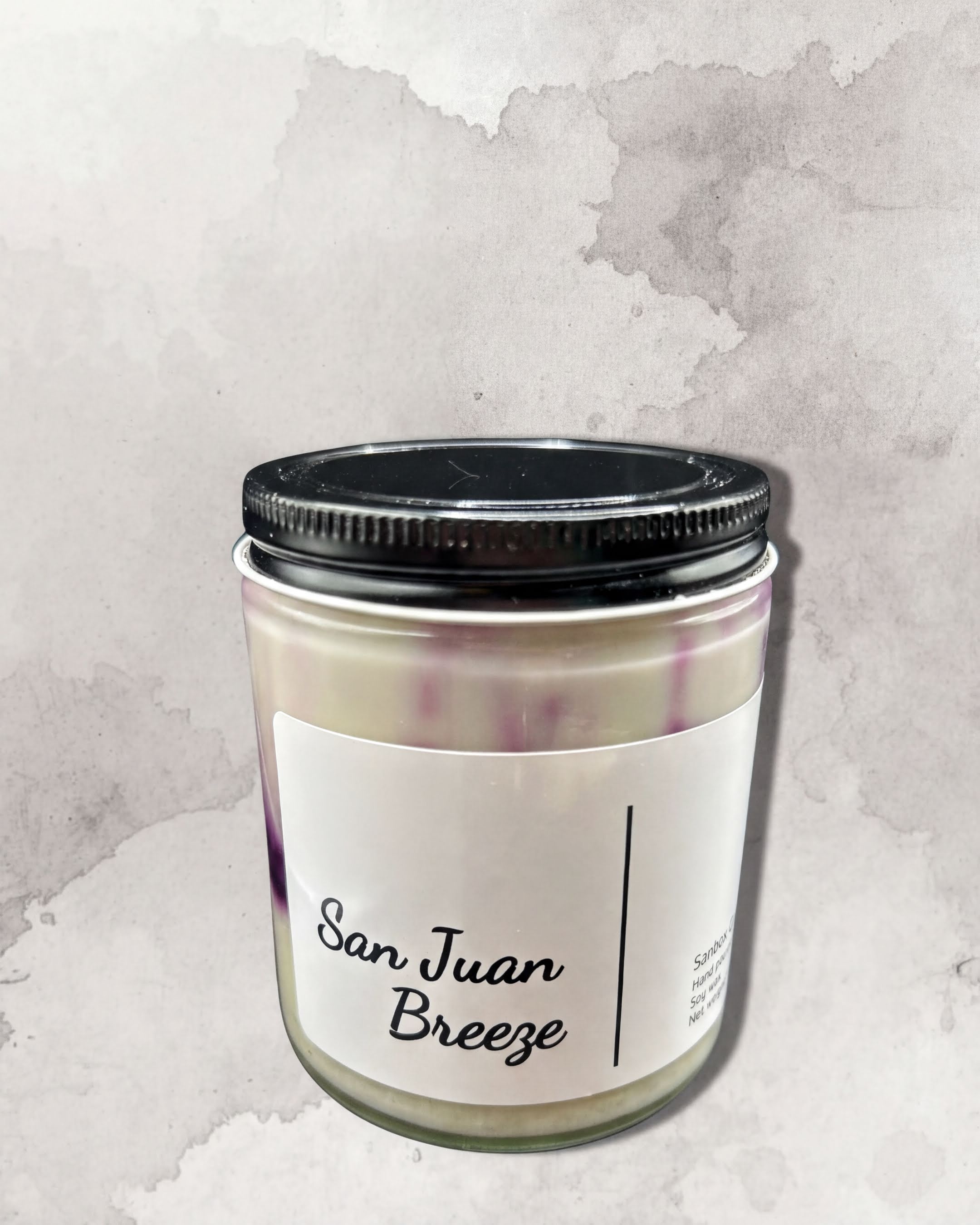 A jar of San Juan Breeze candle against a textured gray background.