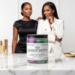Two women standing next to a marble countertop, one wearing a black dress and the other in a white jacket, with a large jar of lavender-colored candle in the center.