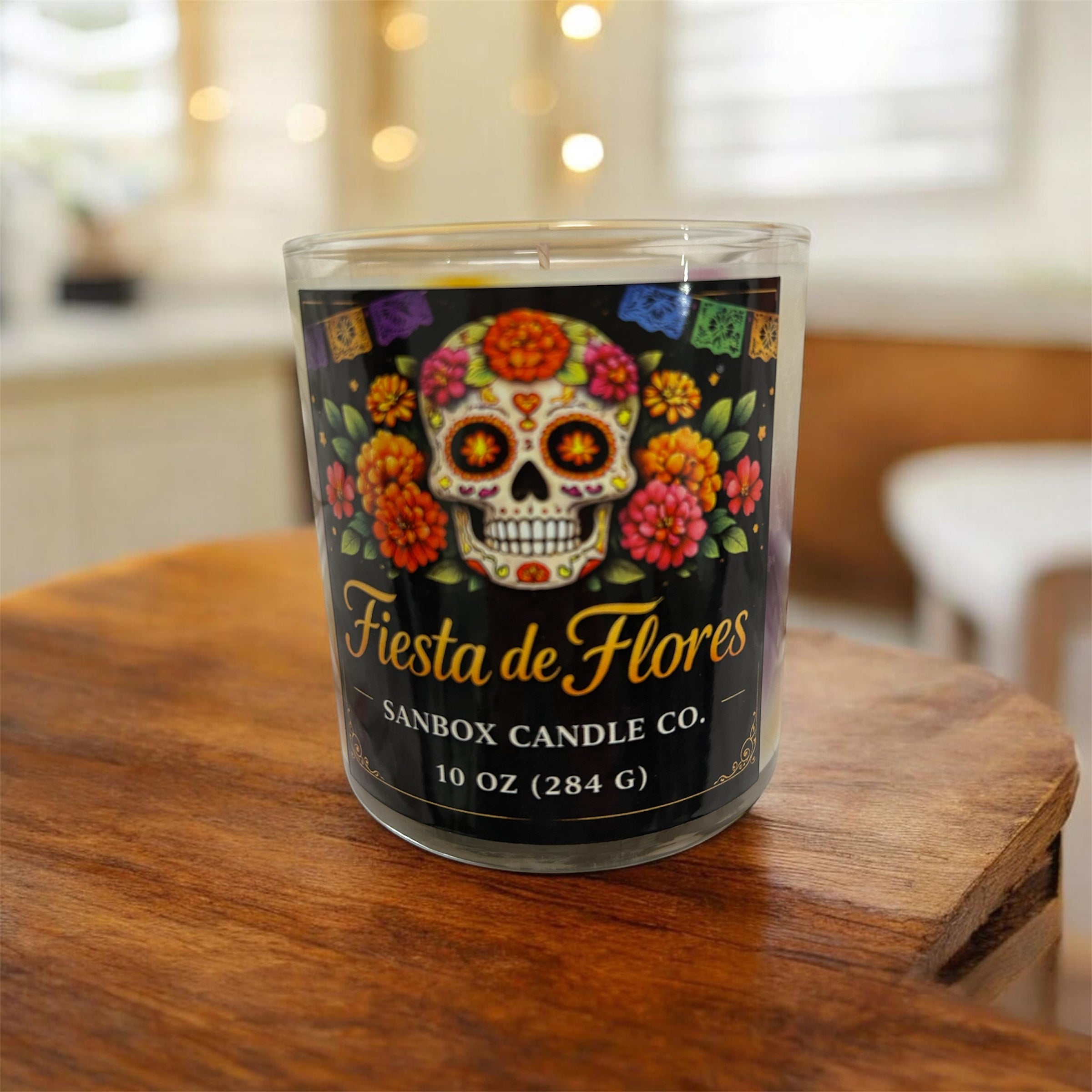 A glass candle holder with a label that reads "Fiesta de Flores" and "SANBOX CANDLE CO."