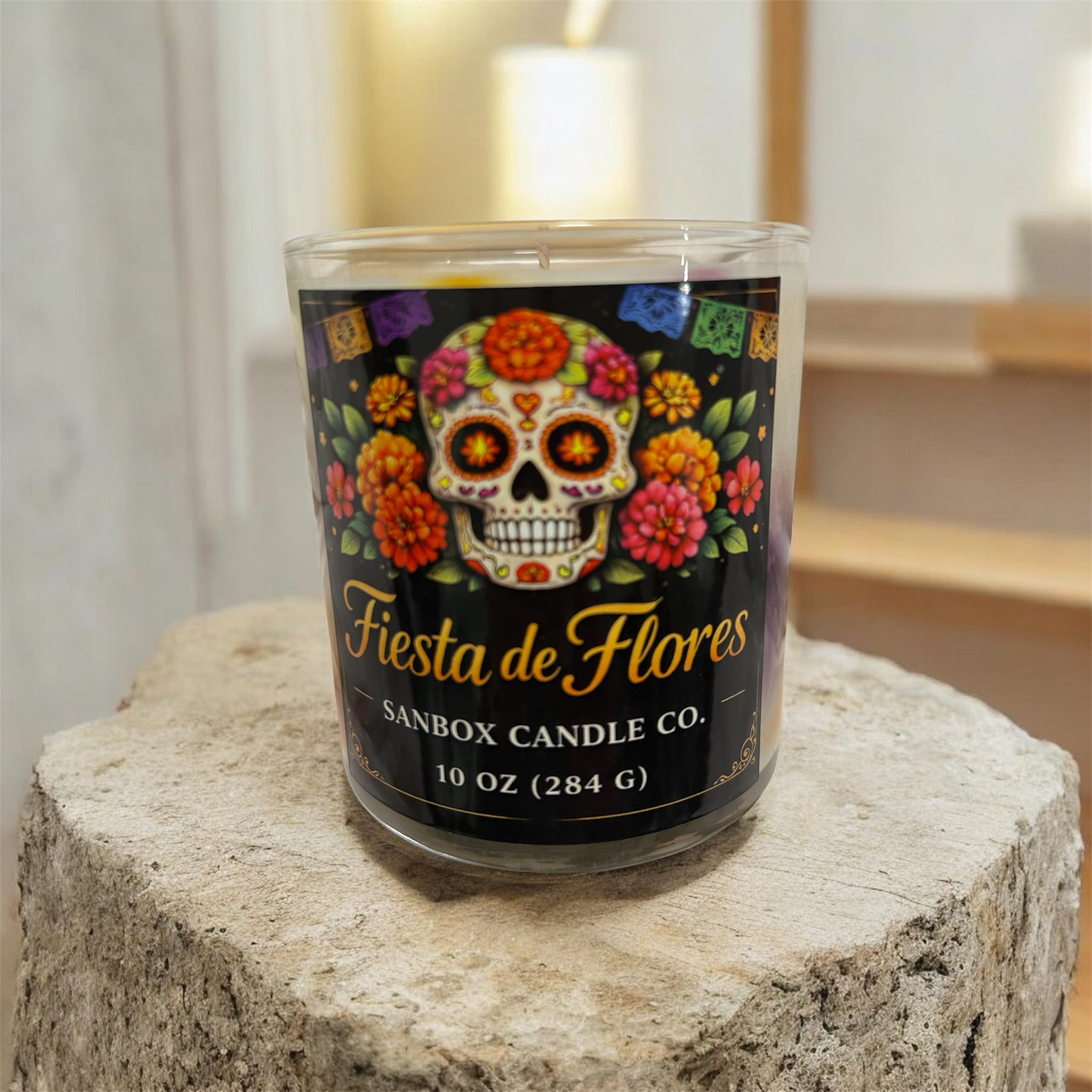 A glass candle holder with a label that reads "Fiesta de Flores" and "SANBOX CANDLE CO."