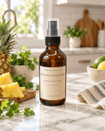 Pineapple & Cilantro room and linen spray in an amber glass bottle with black pump and clear cap, styled with fresh pineapple and cilantro in a kitchen.