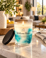 Lit 10 oz Welcome Home soy candle in a clear glass vessel with blue-and-white marbled wax, black lid, and house-and-heart label on a marble table.