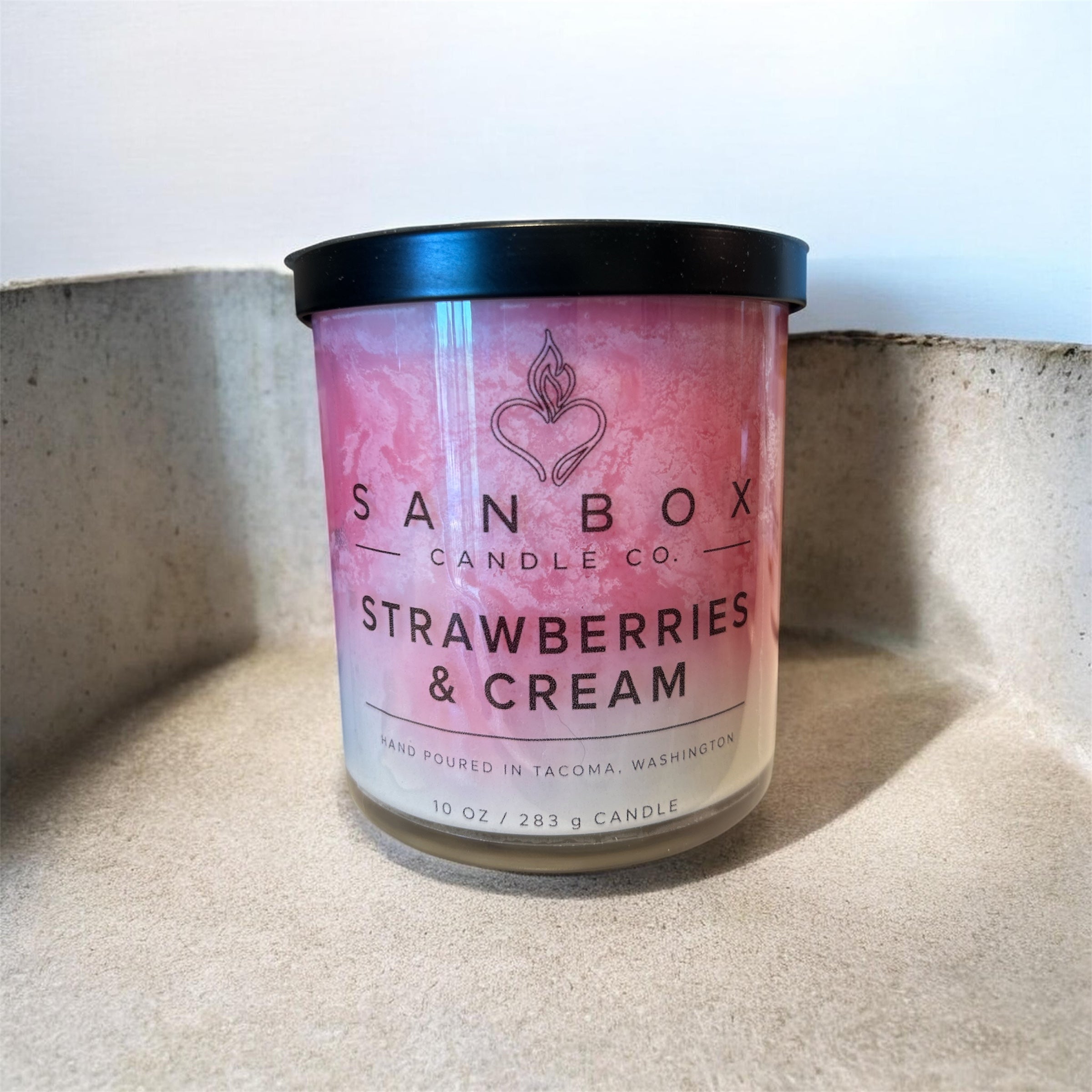 A pink candle labeled "SANBOX CANDLE CO. STRAWBERRIES & CREAM" is sitting on a surface.